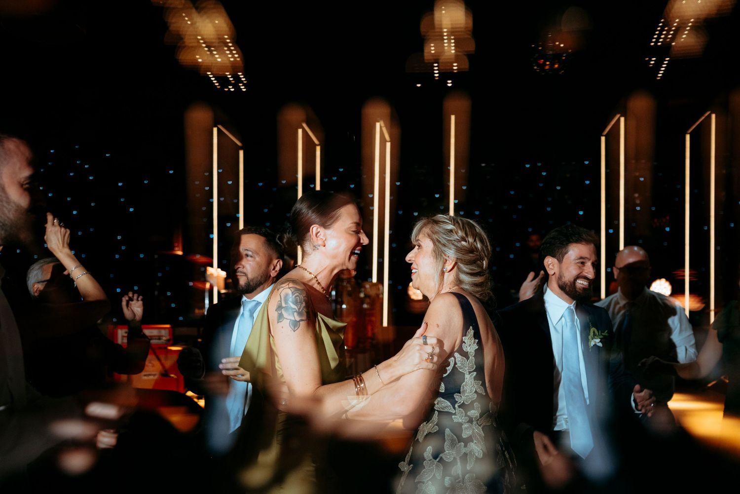 Guests dance joyfully at a wedding reception under warm ambient lighting.
