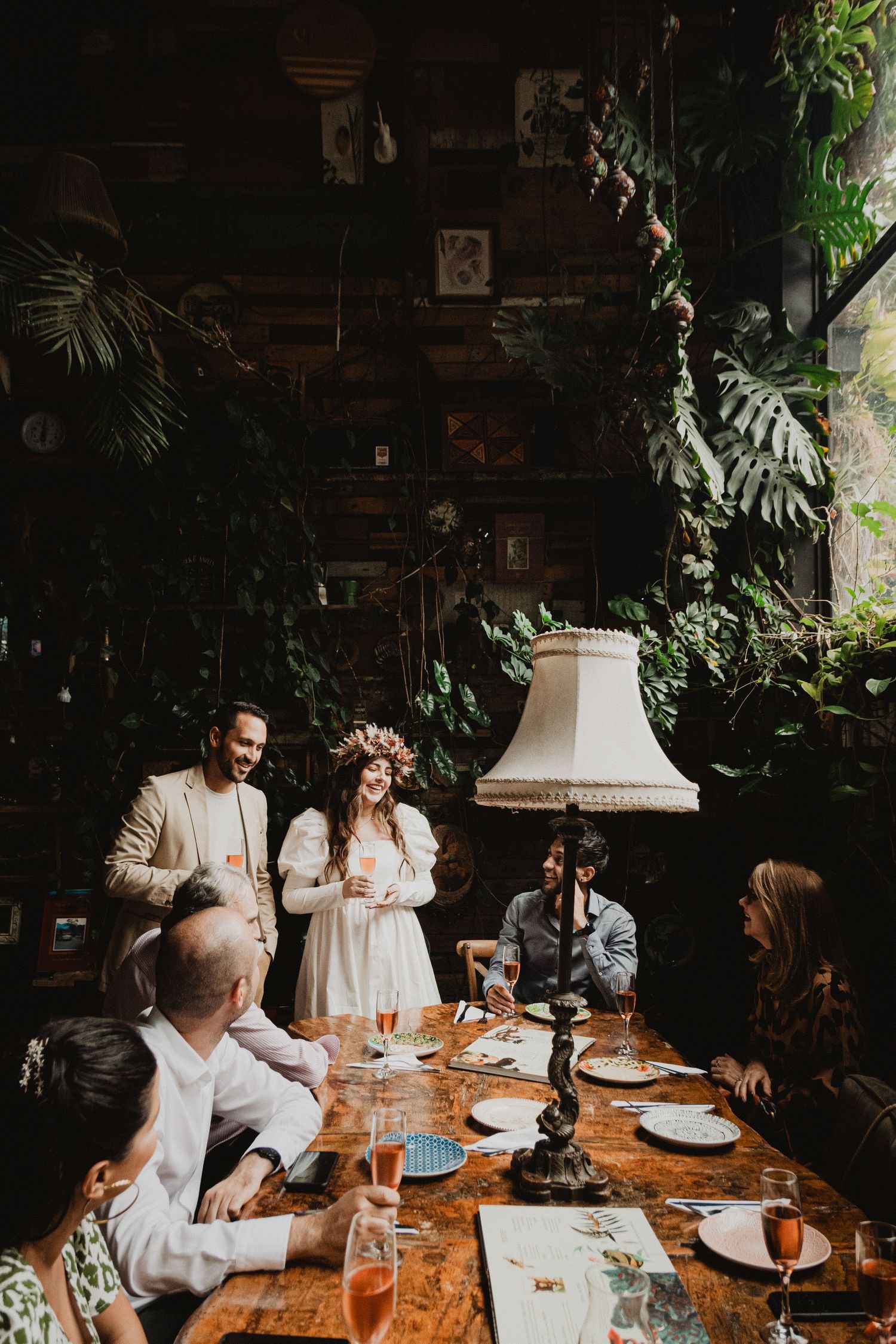 Wedding reception dinner in a lush indoor garden setting with vintage decor.