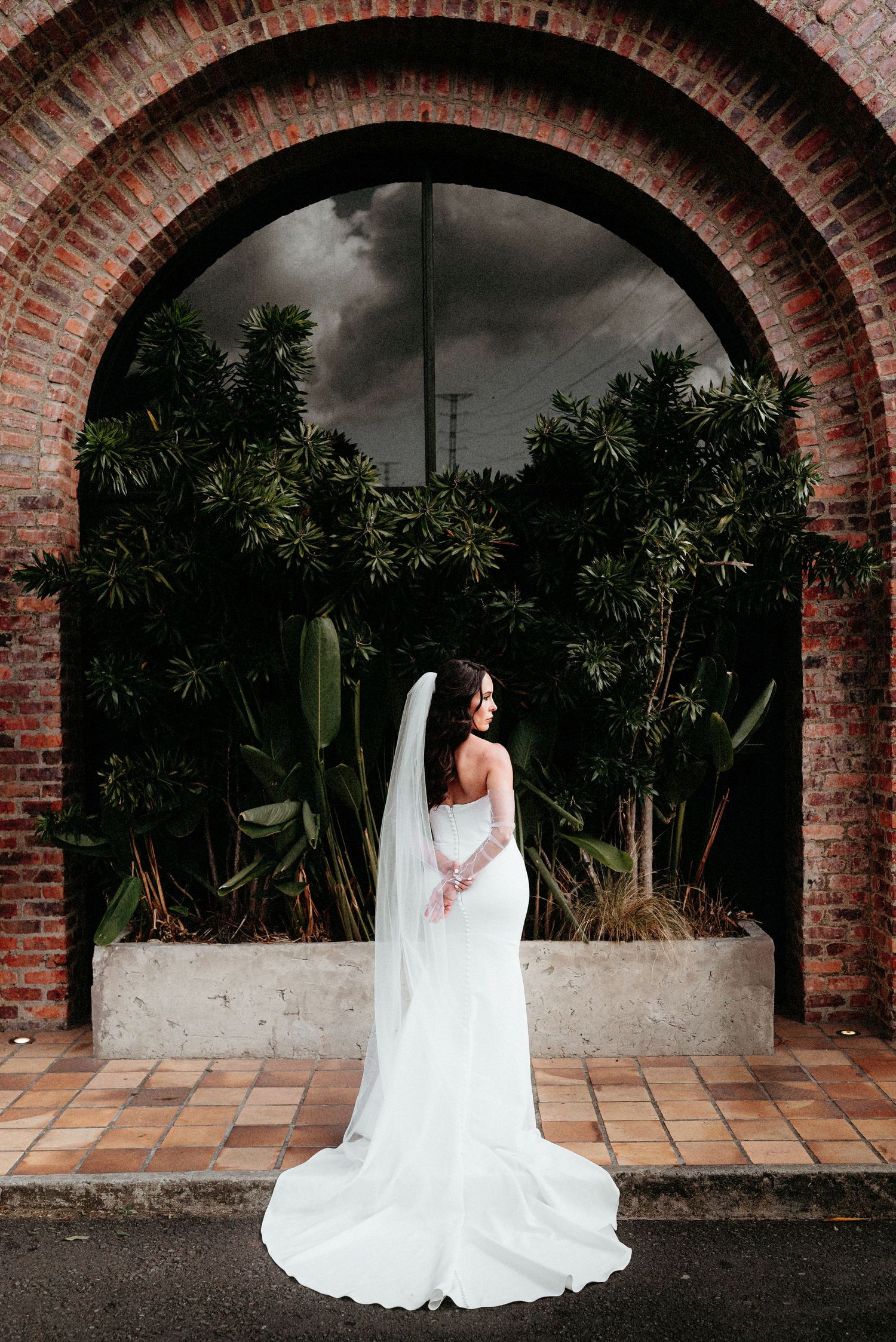 A bride in a white wedding gown poses under brick archways in a garden setting across multiple photos.