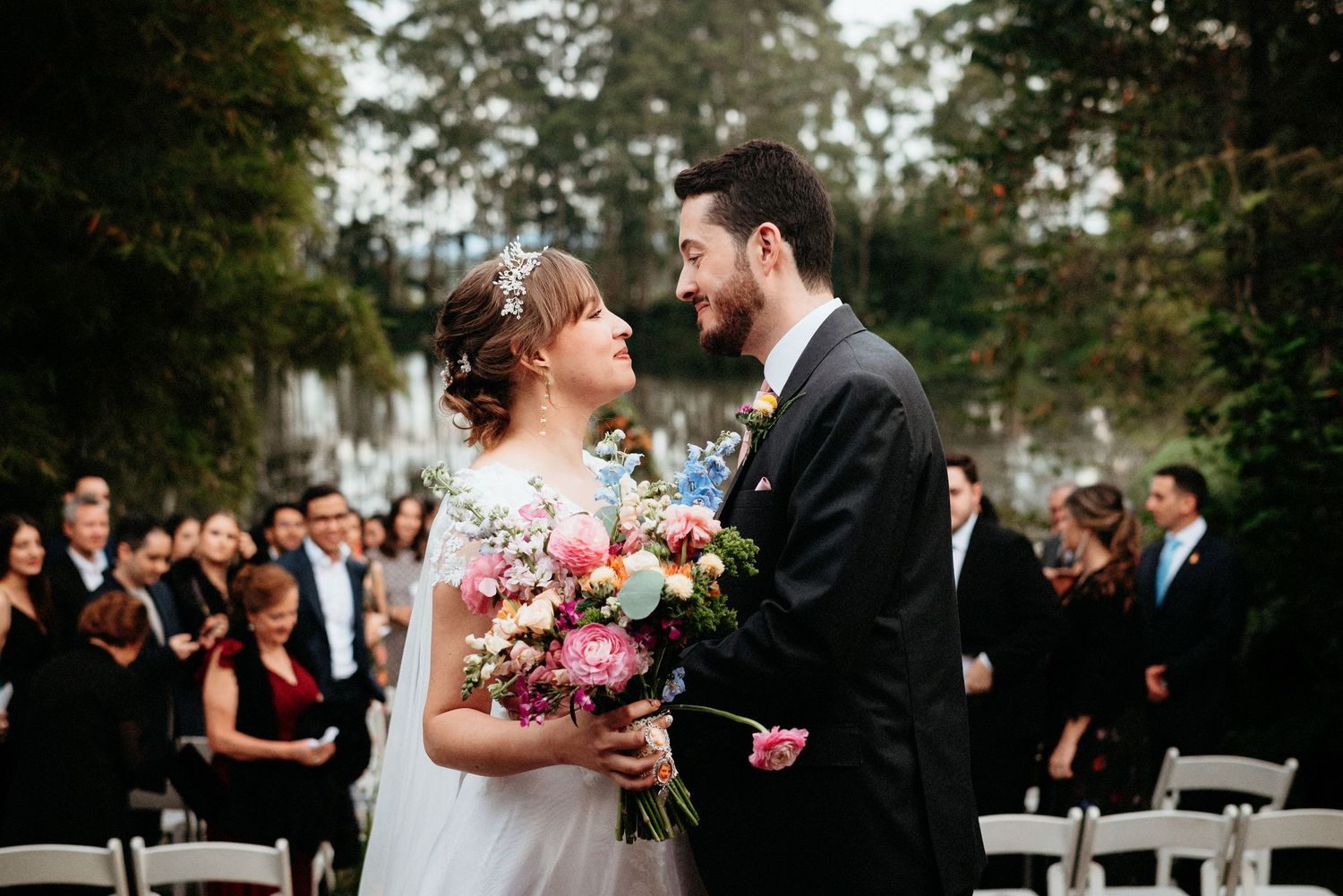 A joyful outdoor wedding ceremony with the couple exchanging looks in front of seated guests.