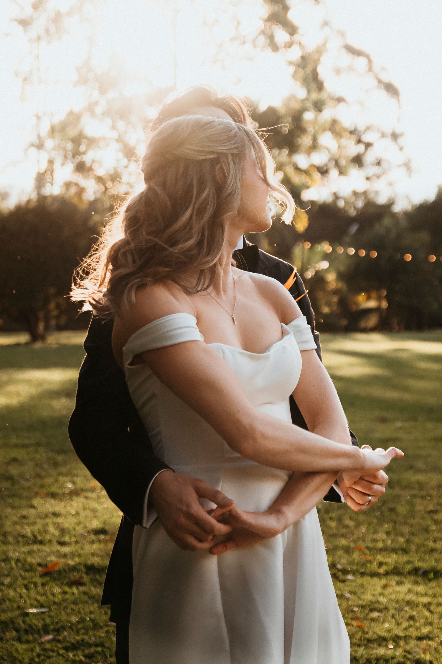 A romantic sunset wedding portrait captured in golden hour light on a grassy lawn.