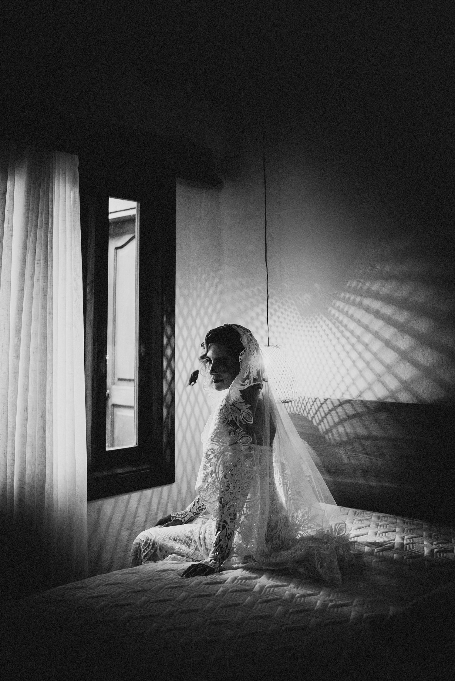 Artistic black and white bridal portrait with dramatic window light and shadow patterns.