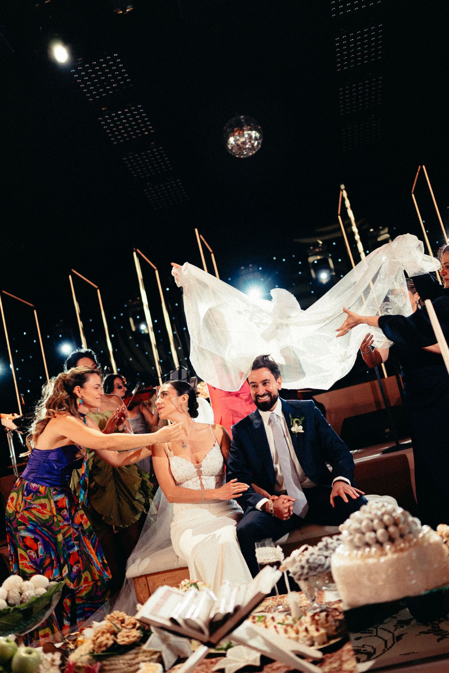 Bride and groom celebrate at wedding reception as guests toss the veil joyfully.