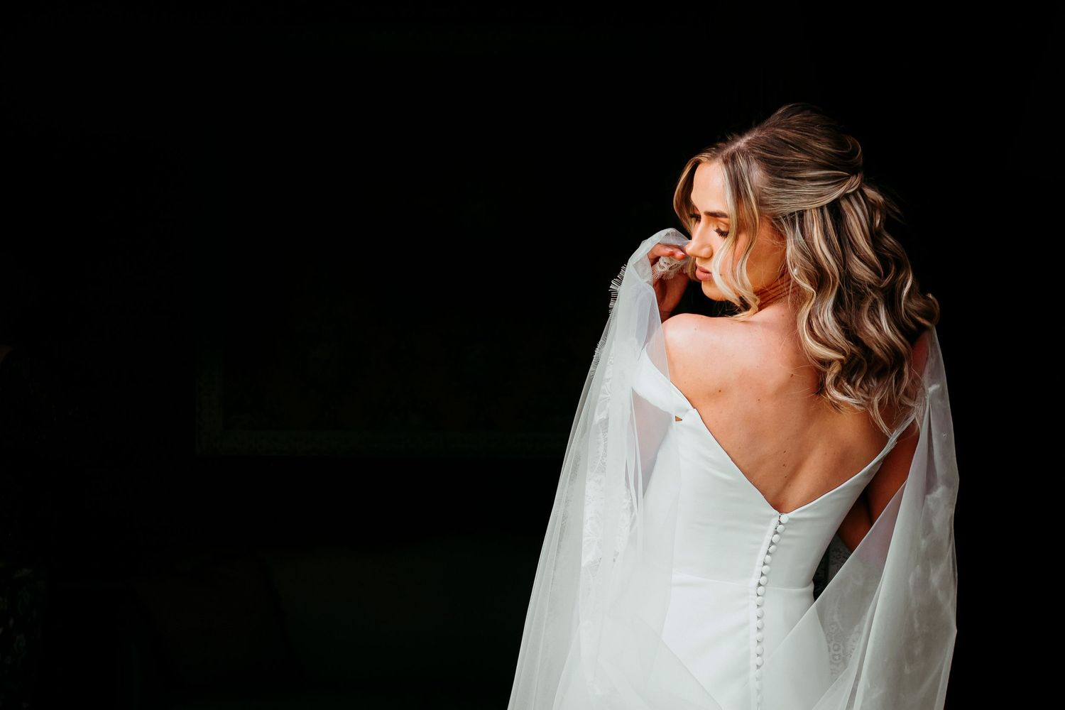 A backlit bridal portrait showing intricate button details on a white wedding dress.