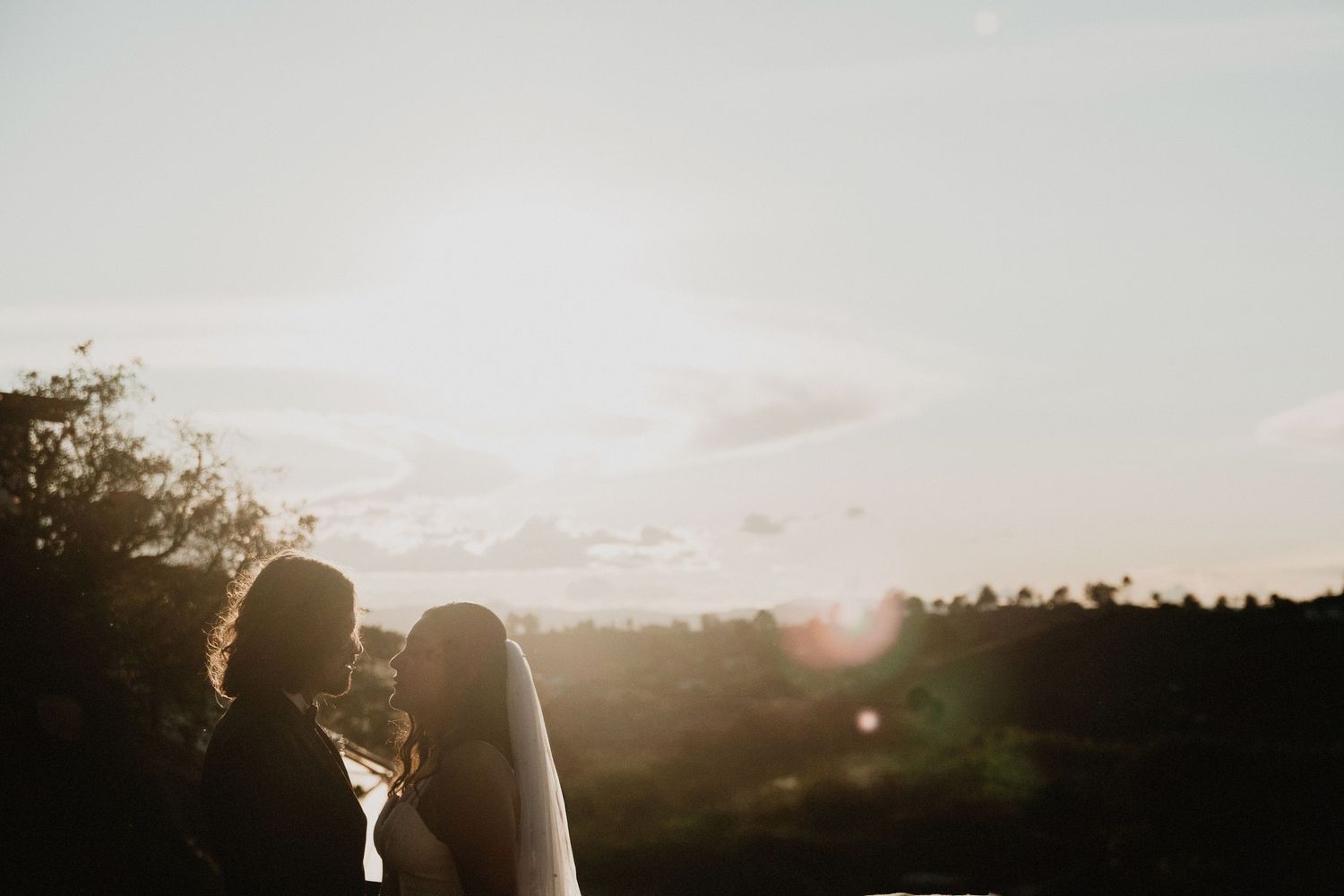 Silhouettes of a couple against a glowing sunset at their outdoor wedding.