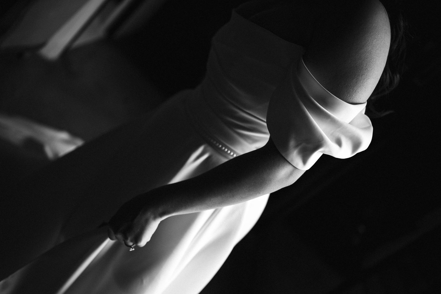 Black and white photo of a bride in an off-shoulder white wedding gown holding a bouquet.