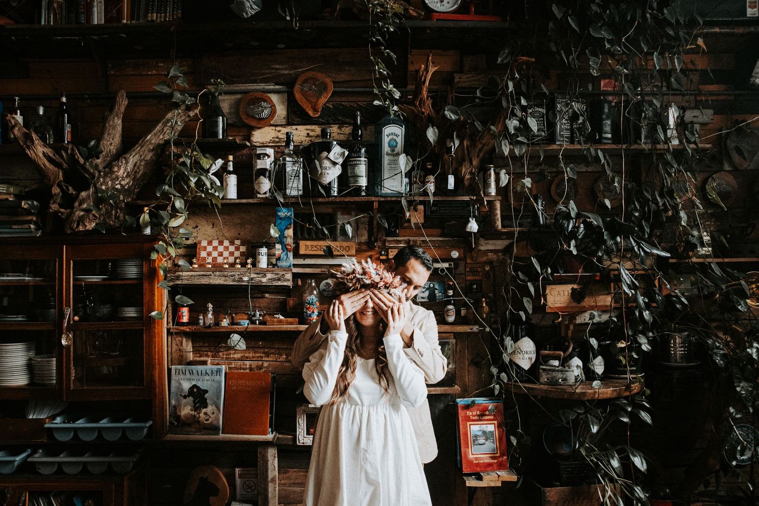 Person in white dress standing in front of rustic shelving filled with vintage decor and plants.