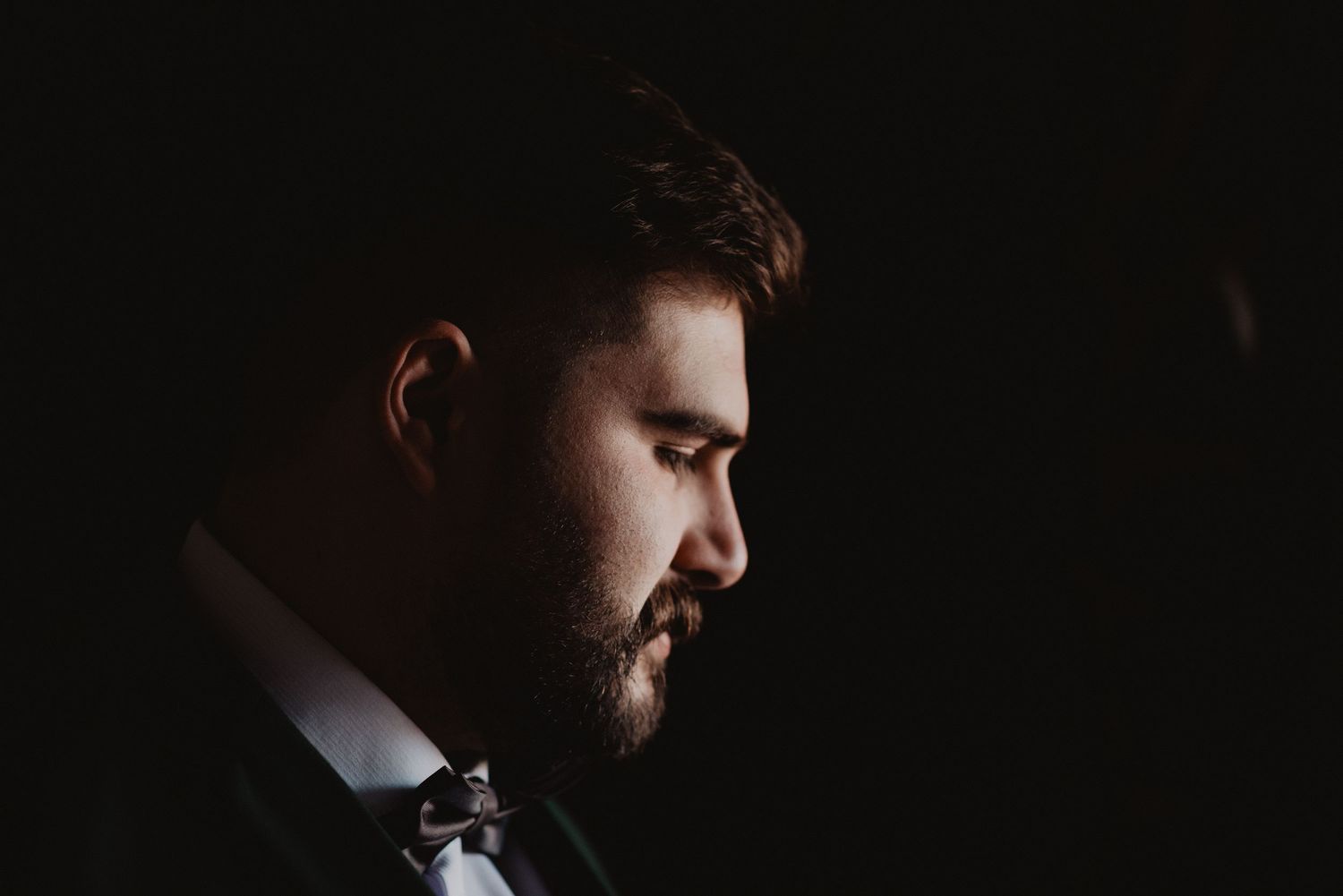 Dramatic side profile portrait in dark moody lighting with formal attire.