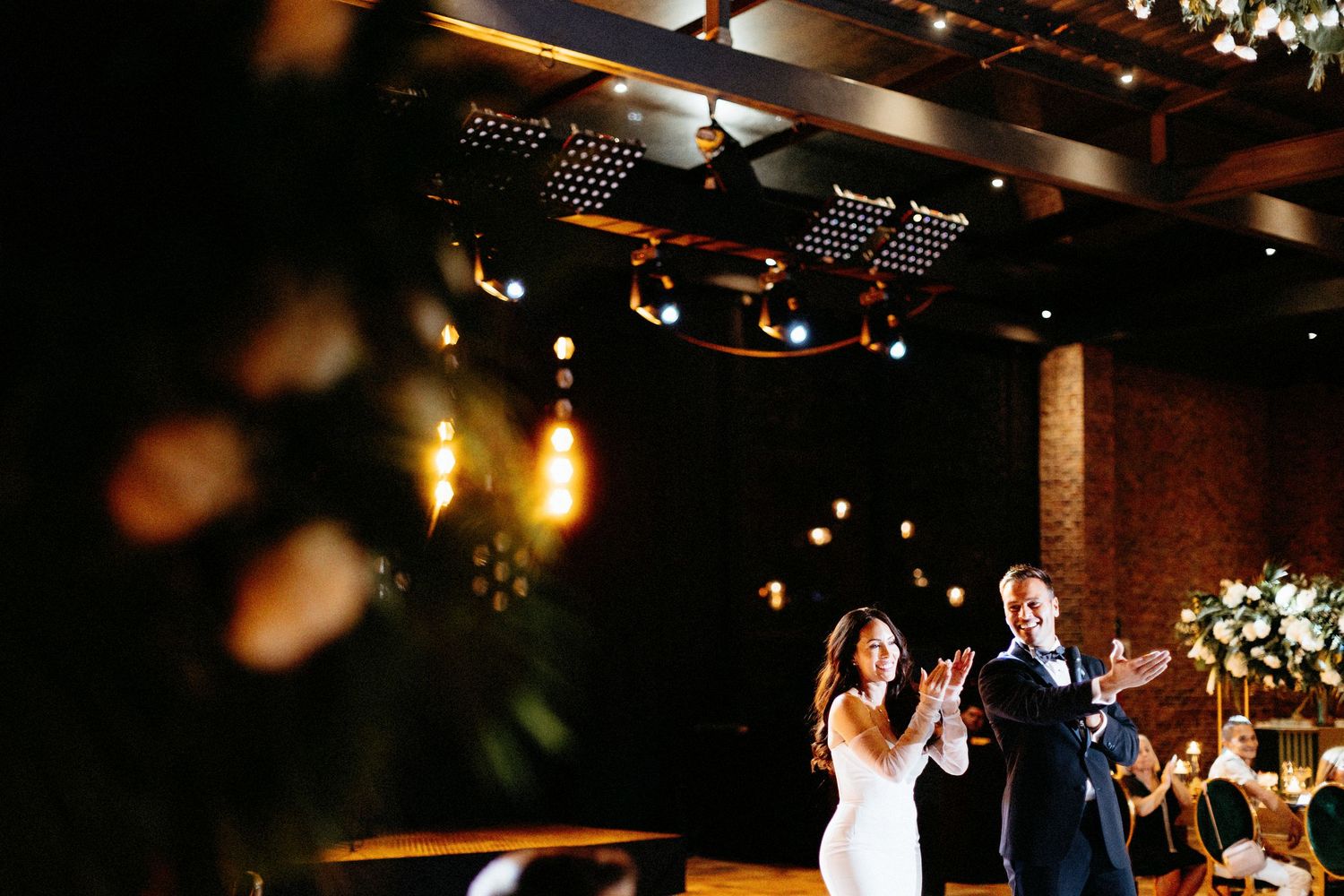 Bride and groom share a joyful first dance in an elegantly lit wedding reception venue with warm Edison bulb lighting.