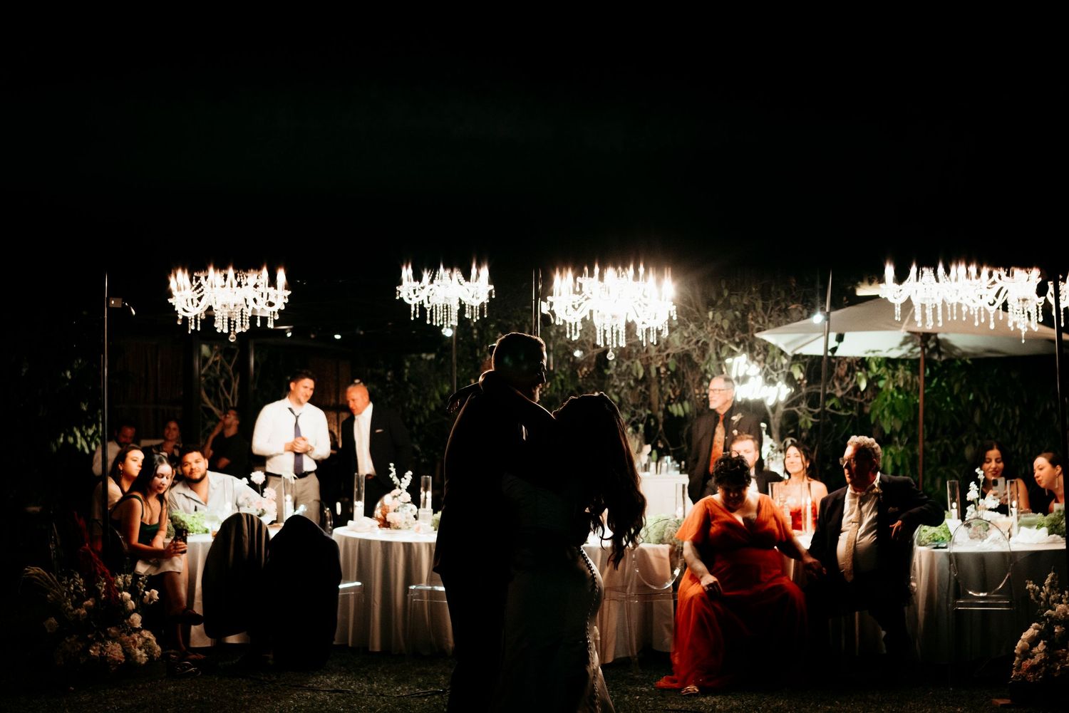 Elegant outdoor wedding reception at night with crystal chandeliers illuminating guest tables.