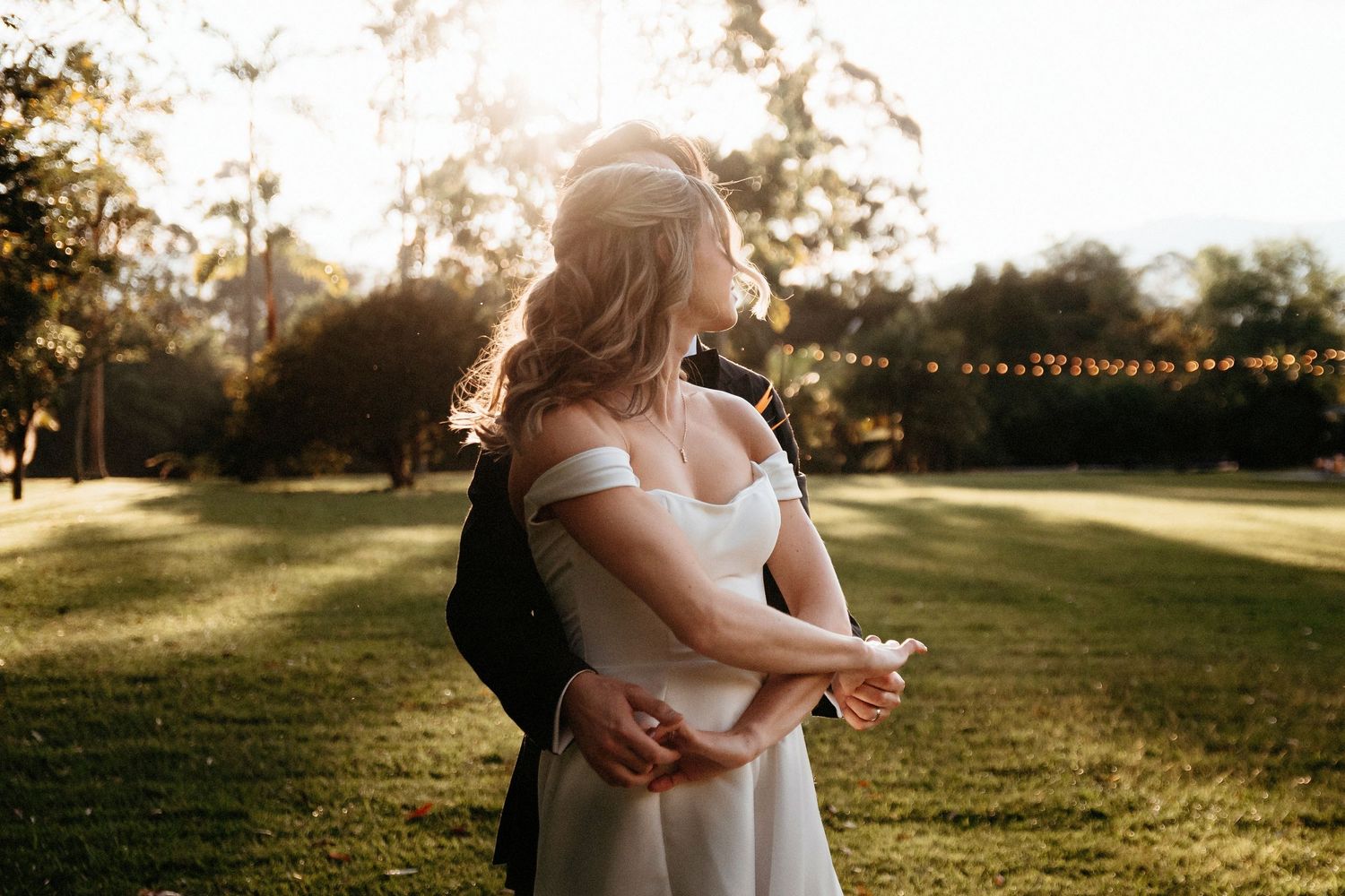 Newlyweds embrace in a golden sunset on their wedding day in a lush garden setting.