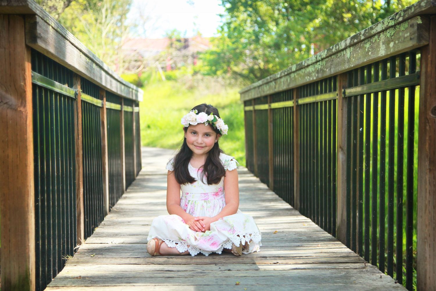 Children Portraits beautiful little girl with flowers in her hair on a wooden bridge