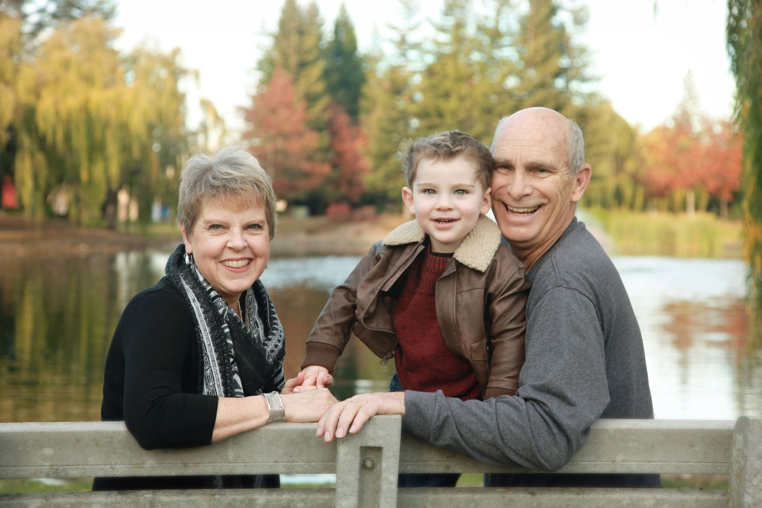 Portrait of grandparents on a park bench with grandson in front of a pond