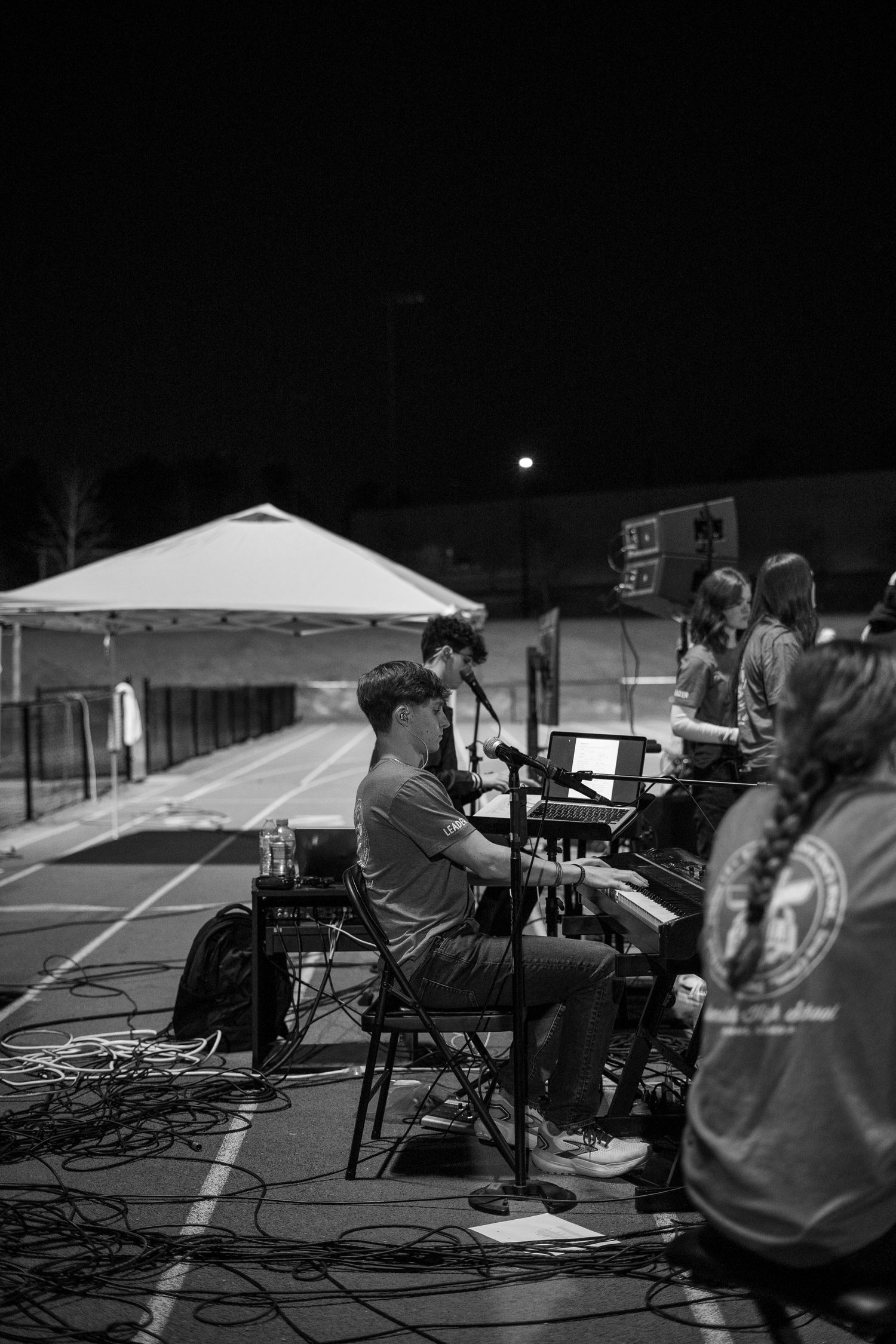 Night scene showing audio technicians working under white tent with equipment setup.