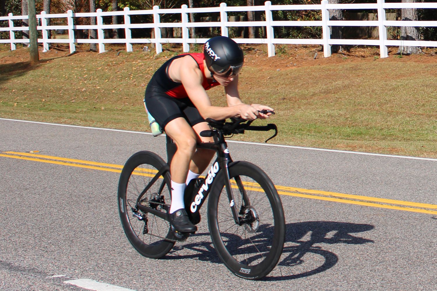 Cyclist in red and black attire racing on a road bike along a country road.