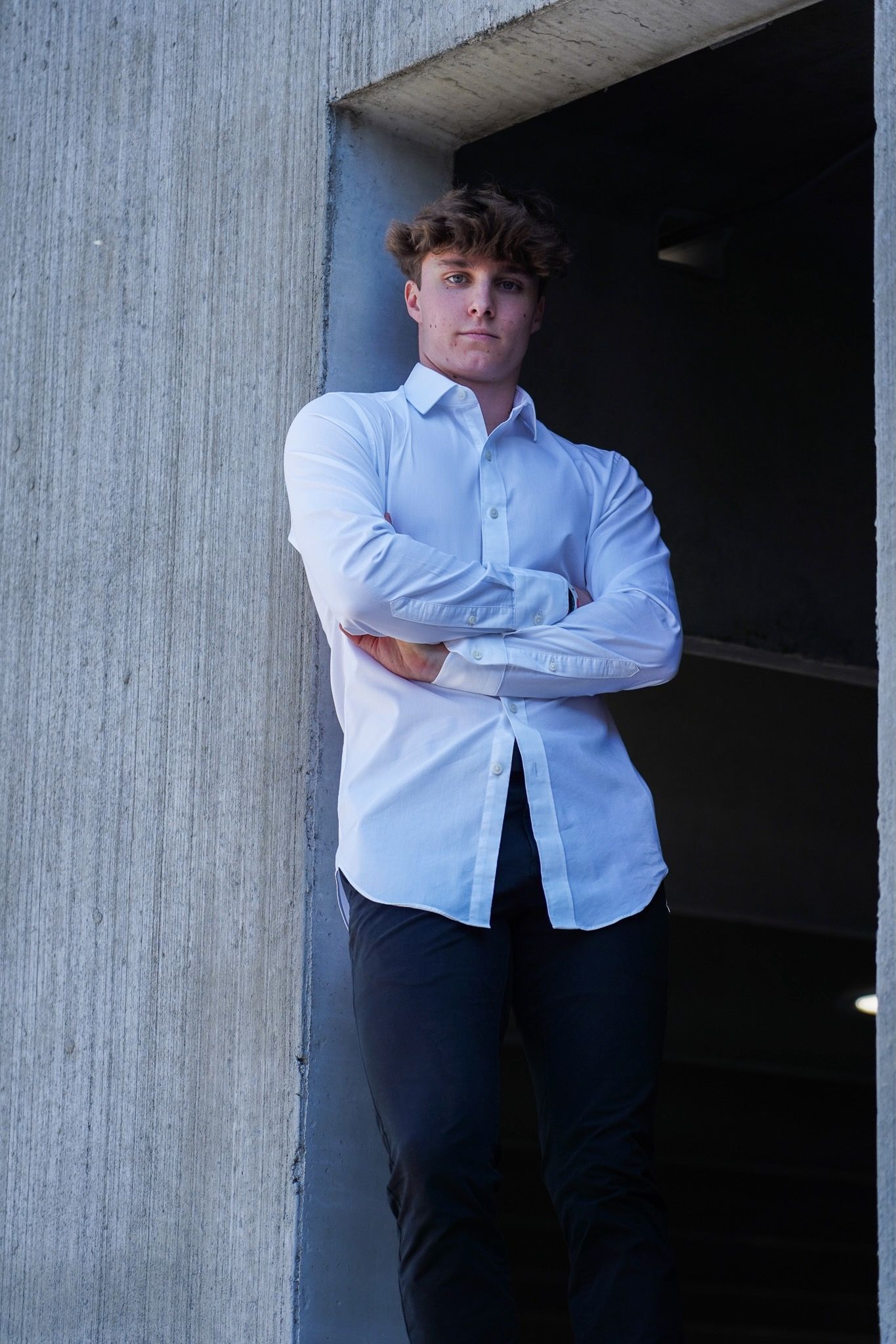 A person wearing a white button-down shirt and dark pants leans against concrete walls in various poses.
