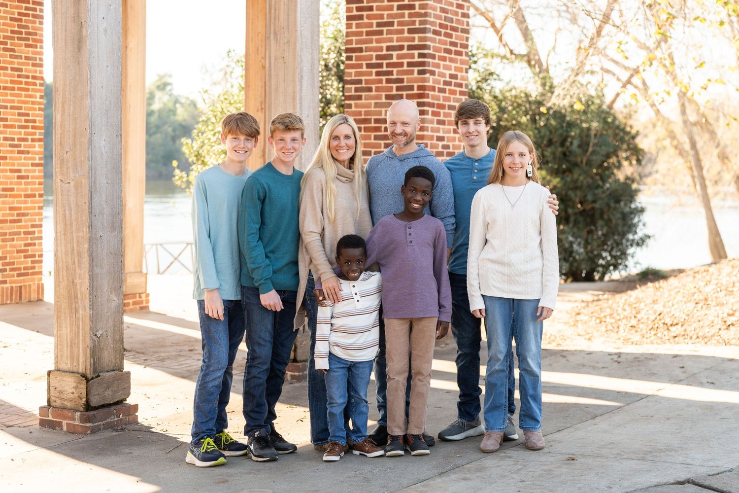 Group portrait of people standing together under brick columns on a sunny day.