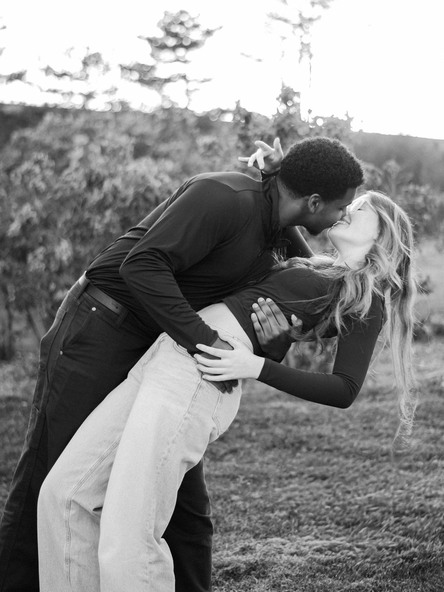 Black and white photo of romantic couple sharing a passionate dip kiss outdoors.