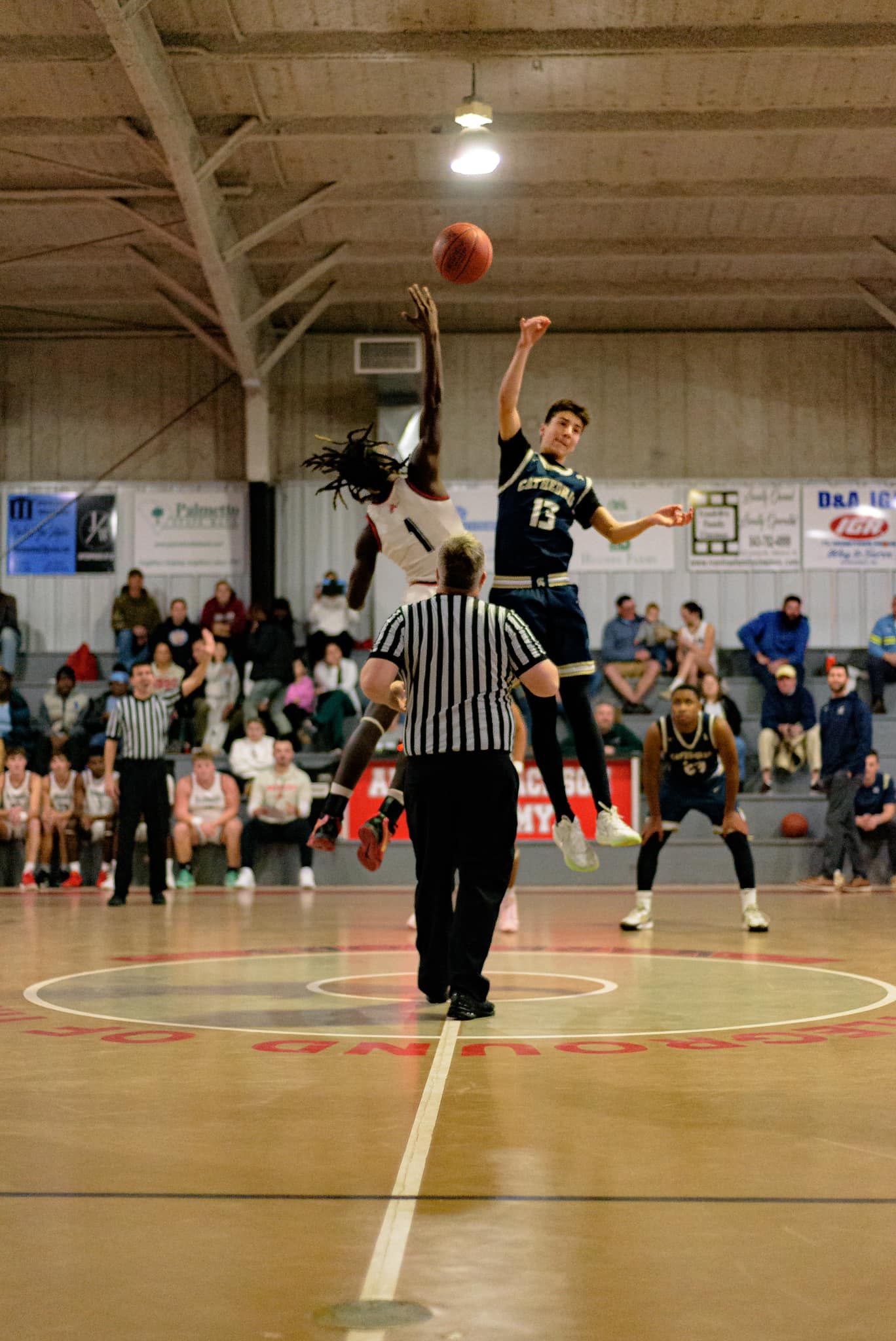 Basketball players jump to compete for the ball during a game in an indoor gymnasium.