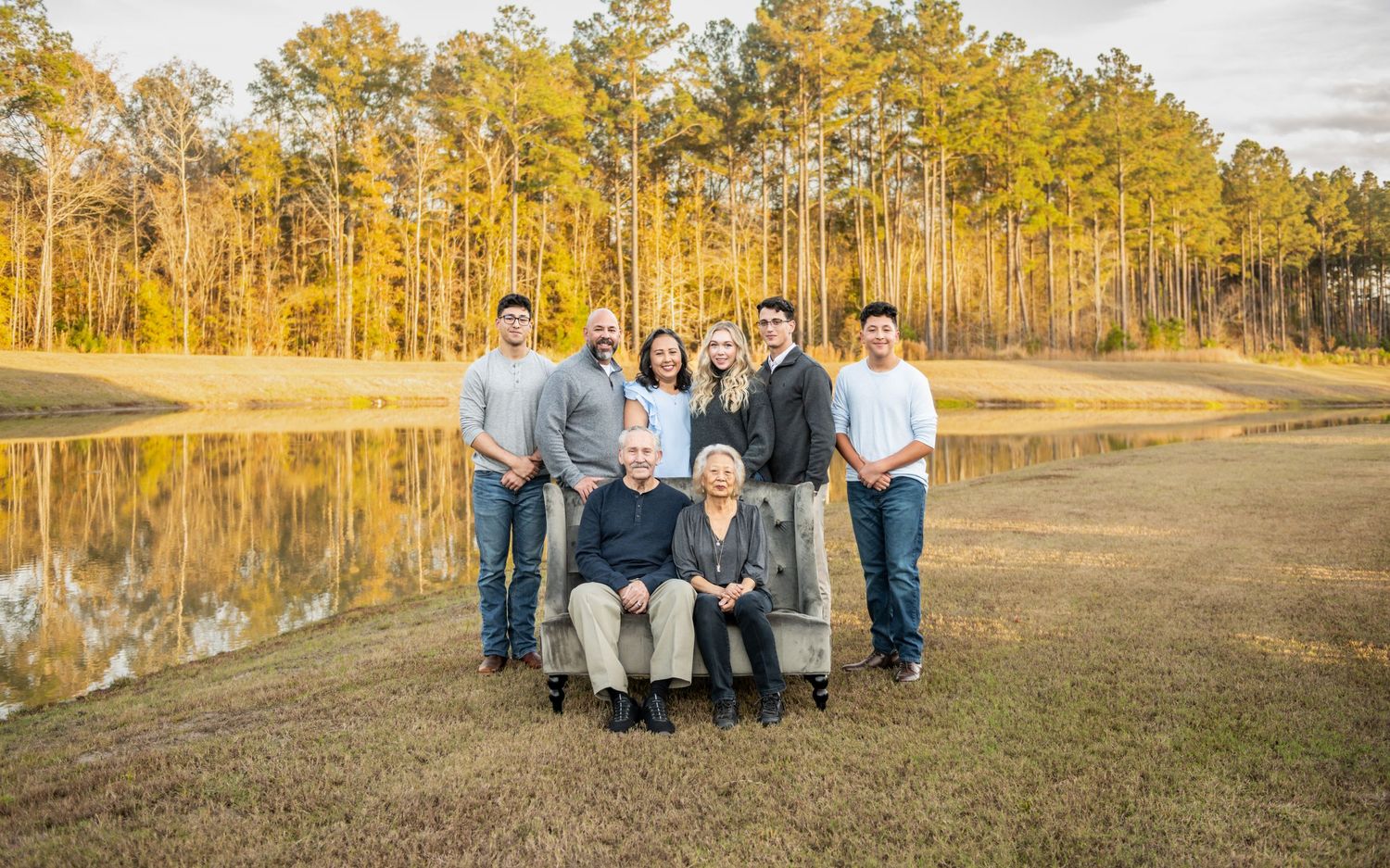 A group poses together by a serene lake with golden pine trees reflecting in the water during sunset.