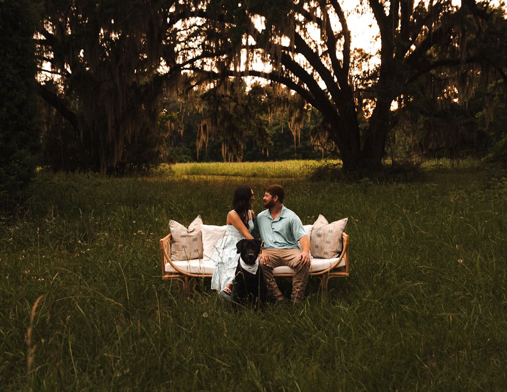 A couple sits together on a grassy field at sunset, creating a romantic silhouette against the warm evening sky.