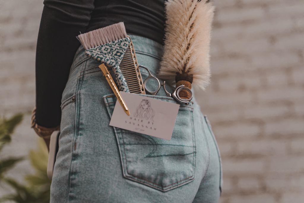 Close-up of pastel pink leather wallet and silver scissors tucked into back pocket of light wash denim jeans.