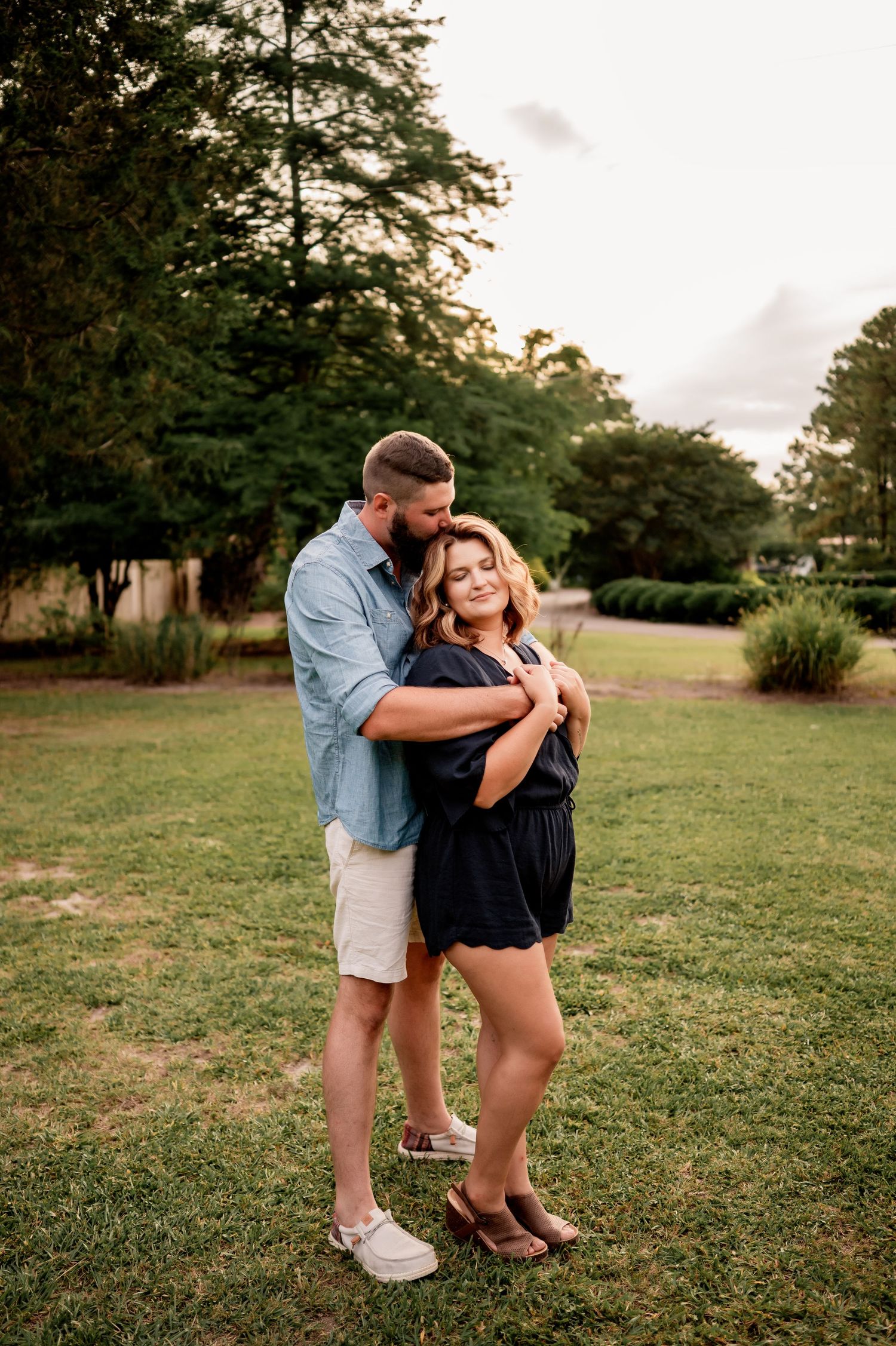 A couple shares a tender moment together in a grassy field during sunset.