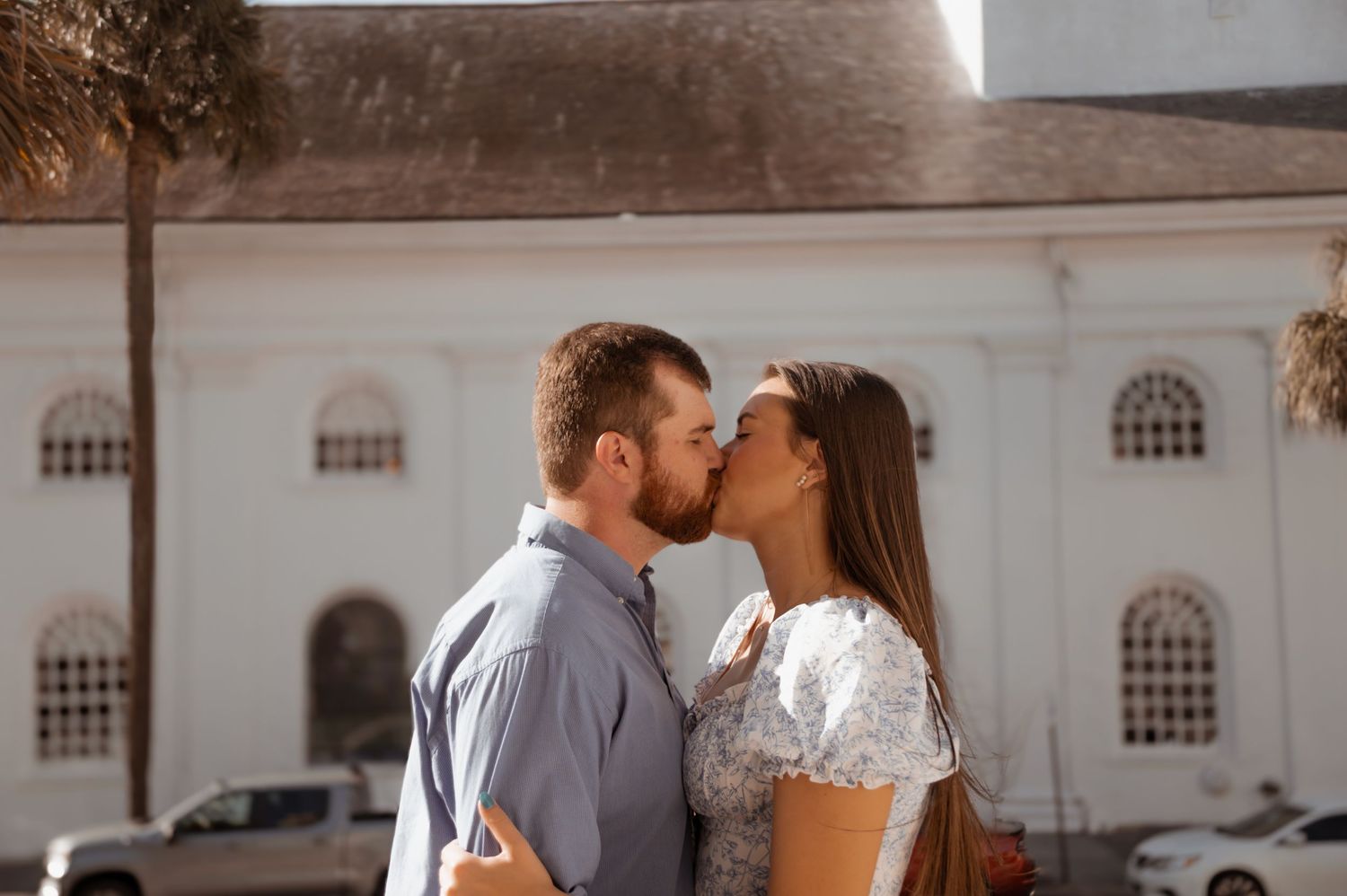 A couple shares a romantic kiss in front of a white church building during their wedding day.