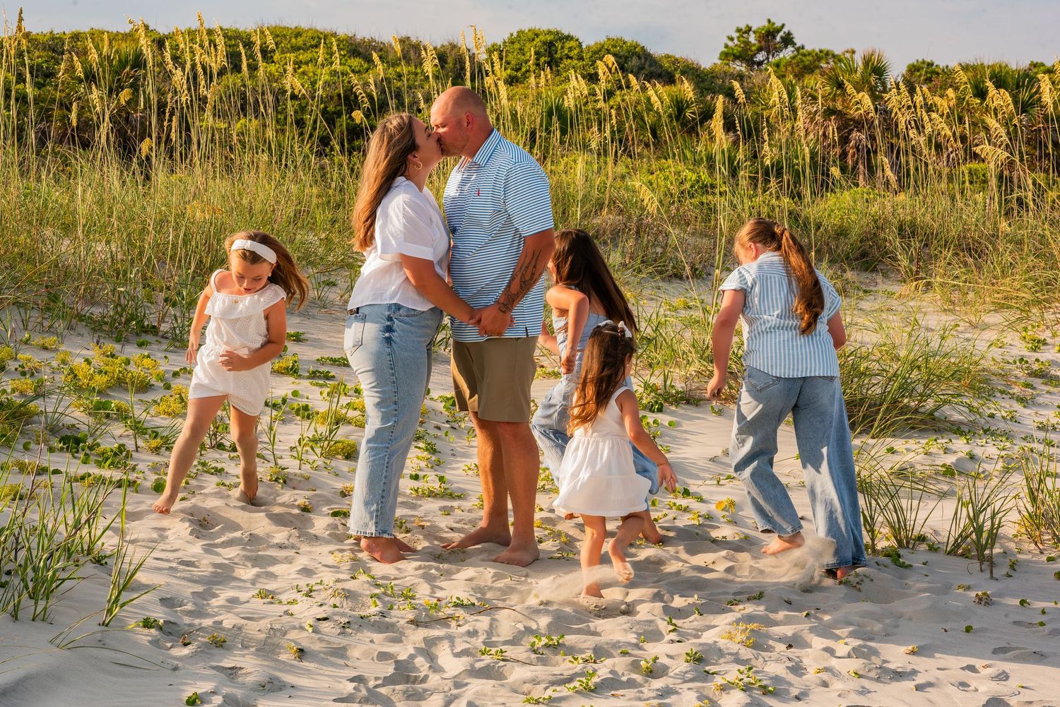 People walking together on a sandy beach path through sea oats and dunes during golden hour.