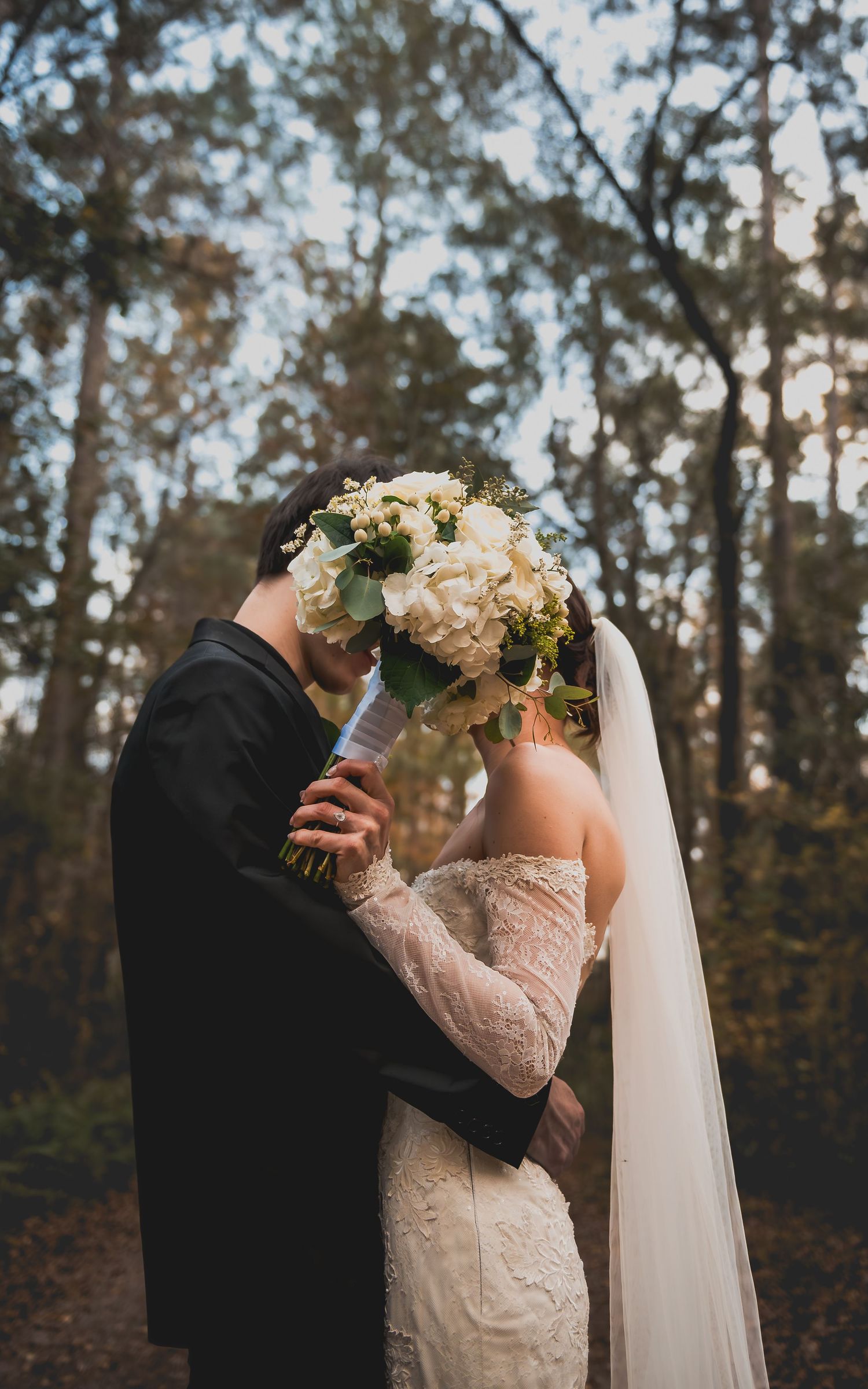 Romantic wedding couple shares intimate dance moment in a wooded outdoor setting with autumn trees in background.
