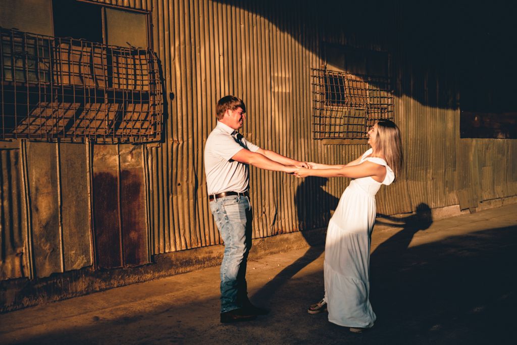 A couple dances together at sunset against an industrial backdrop with metal walls and shadows.
