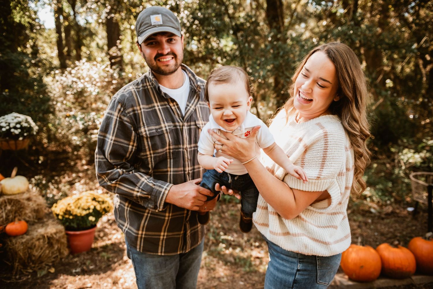 A family enjoys a fall photoshoot together outdoors surrounded by autumn pumpkins and golden sunlight.