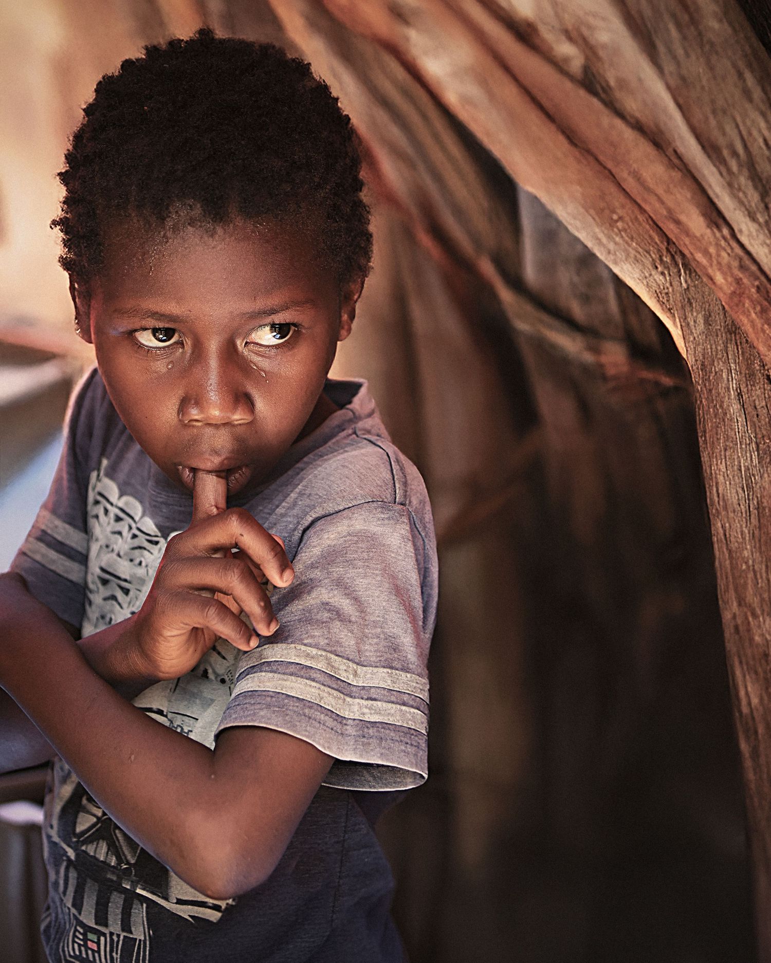 A close-up portrait of a young African girl with a tear rolling down her cheek, standing in a poor neighborhood during a funeral ceremony.