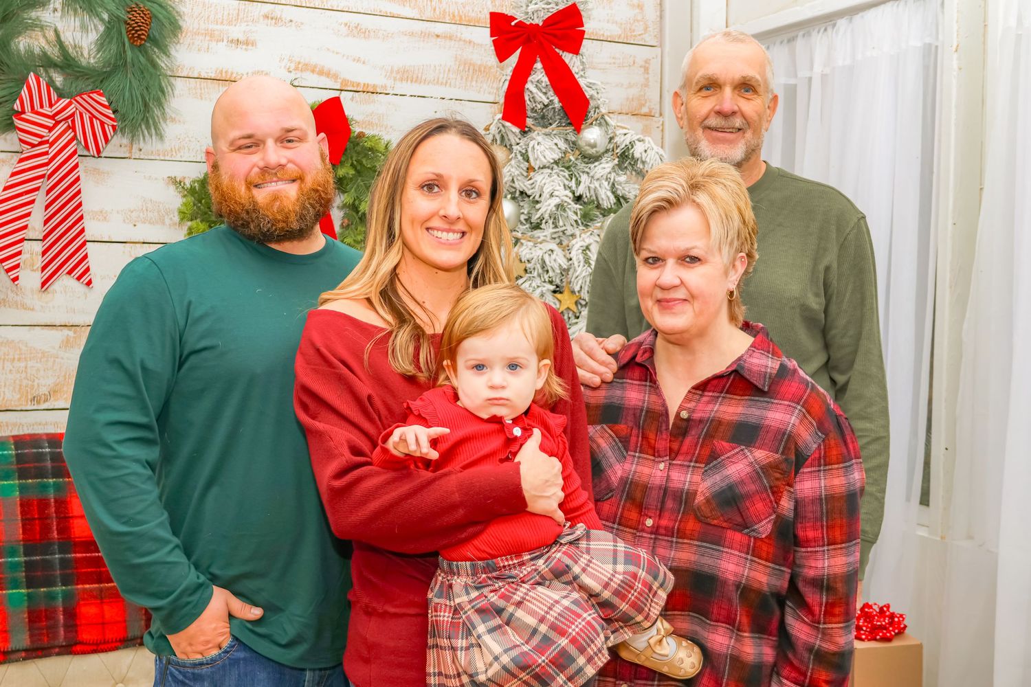 Family members pose together for Christmas photo with wreath and holiday decorations.
