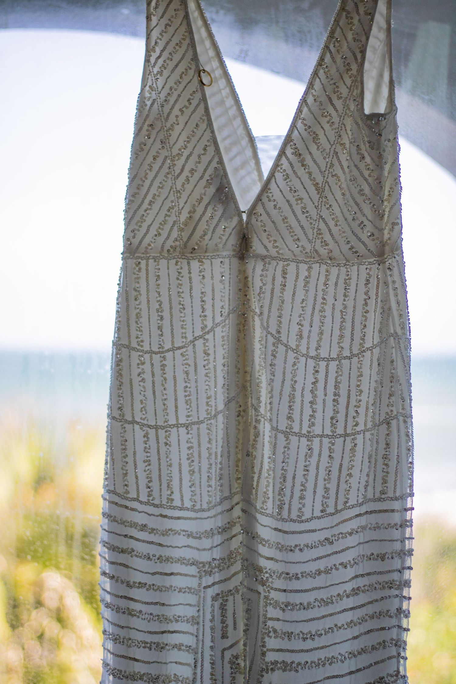 A white beaded wedding dress with intricate pattern detail hanging outdoors.