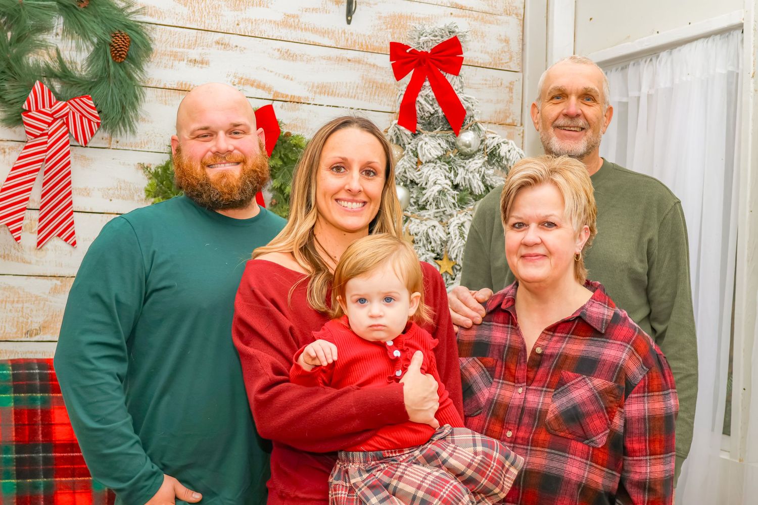 A festive family holiday photo with Christmas decor including a wreath and candy cane against a light background.