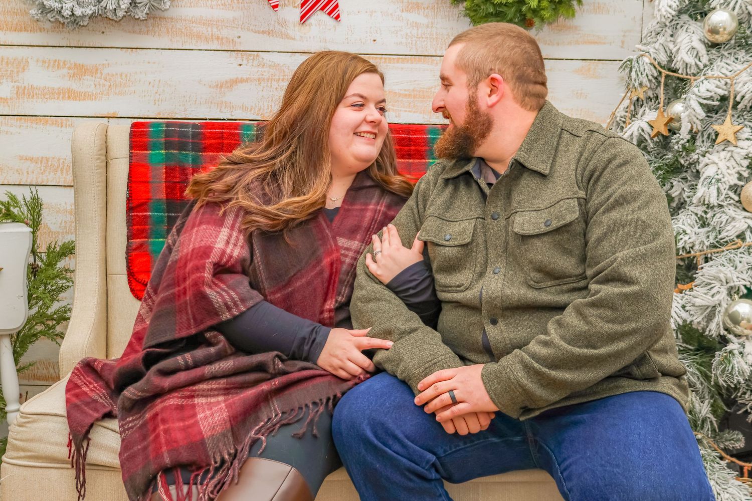 Candid holiday photo of couple laughing on bench with Christmas decorations in background.
