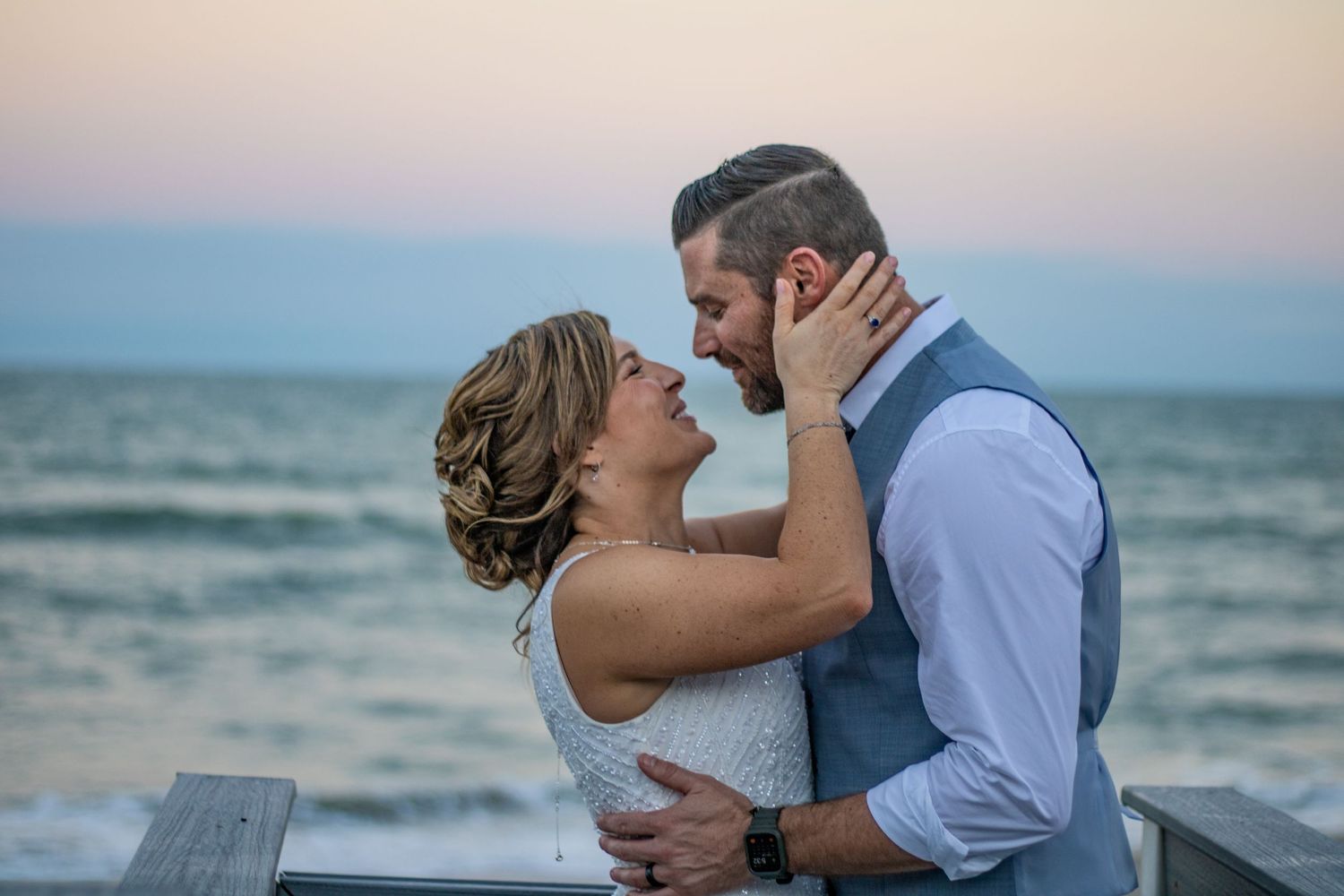 Romantic sunset portrait of newlyweds embracing by the ocean.
