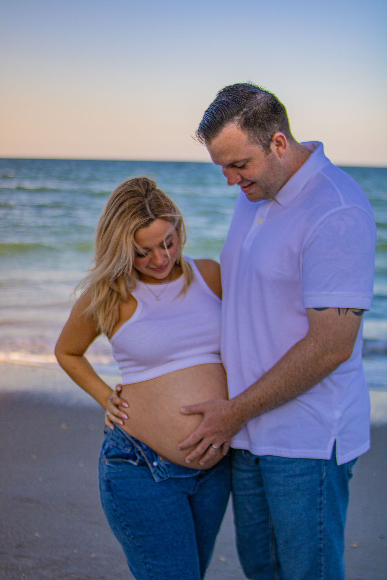 Couple shares tender moment during beachside maternity photoshoot.