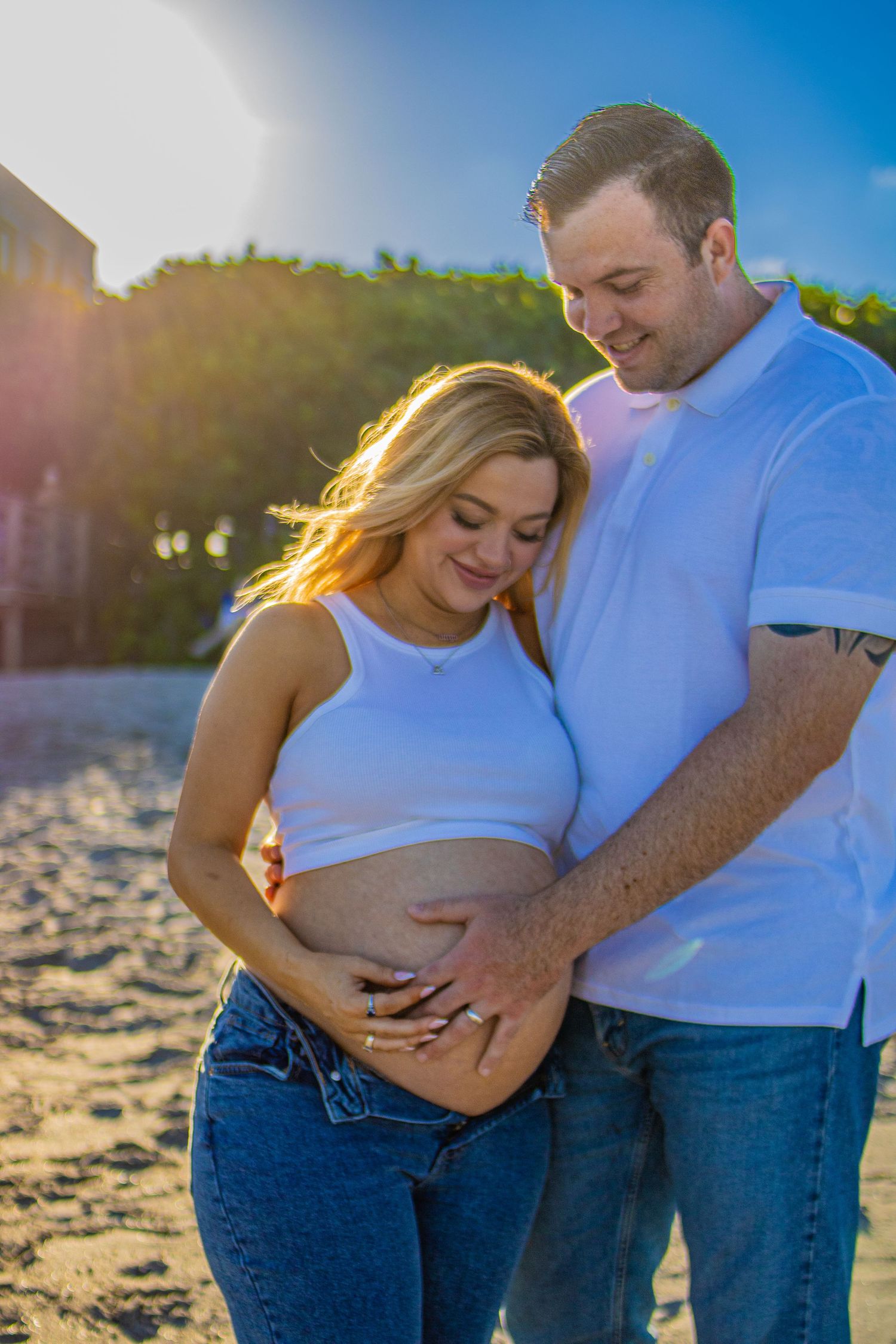 Expectant couple shares tender moment on beach at sunset as they cradle pregnancy bump.