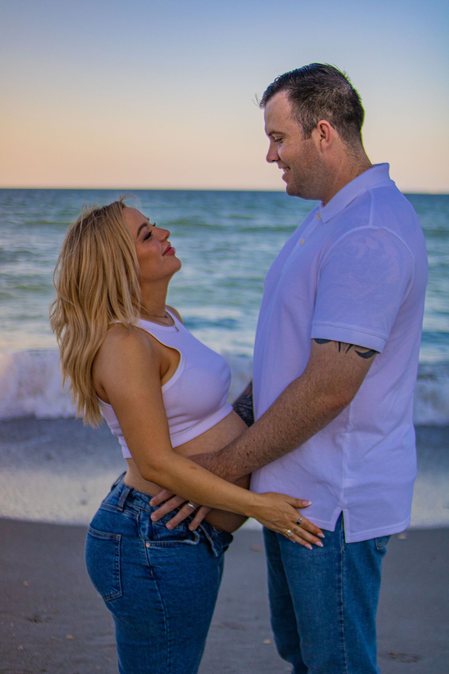 Romantic maternity photo of couple embracing on beach at dusk.