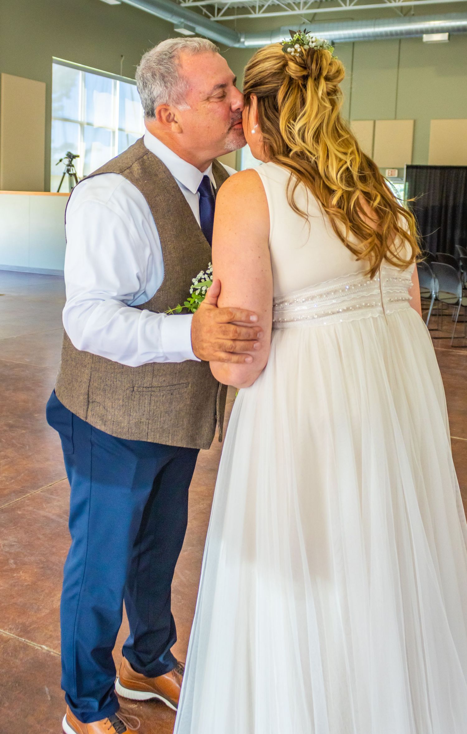 A tender moment captured between a couple at their wedding, with the bride in white and groom in a brown vest.