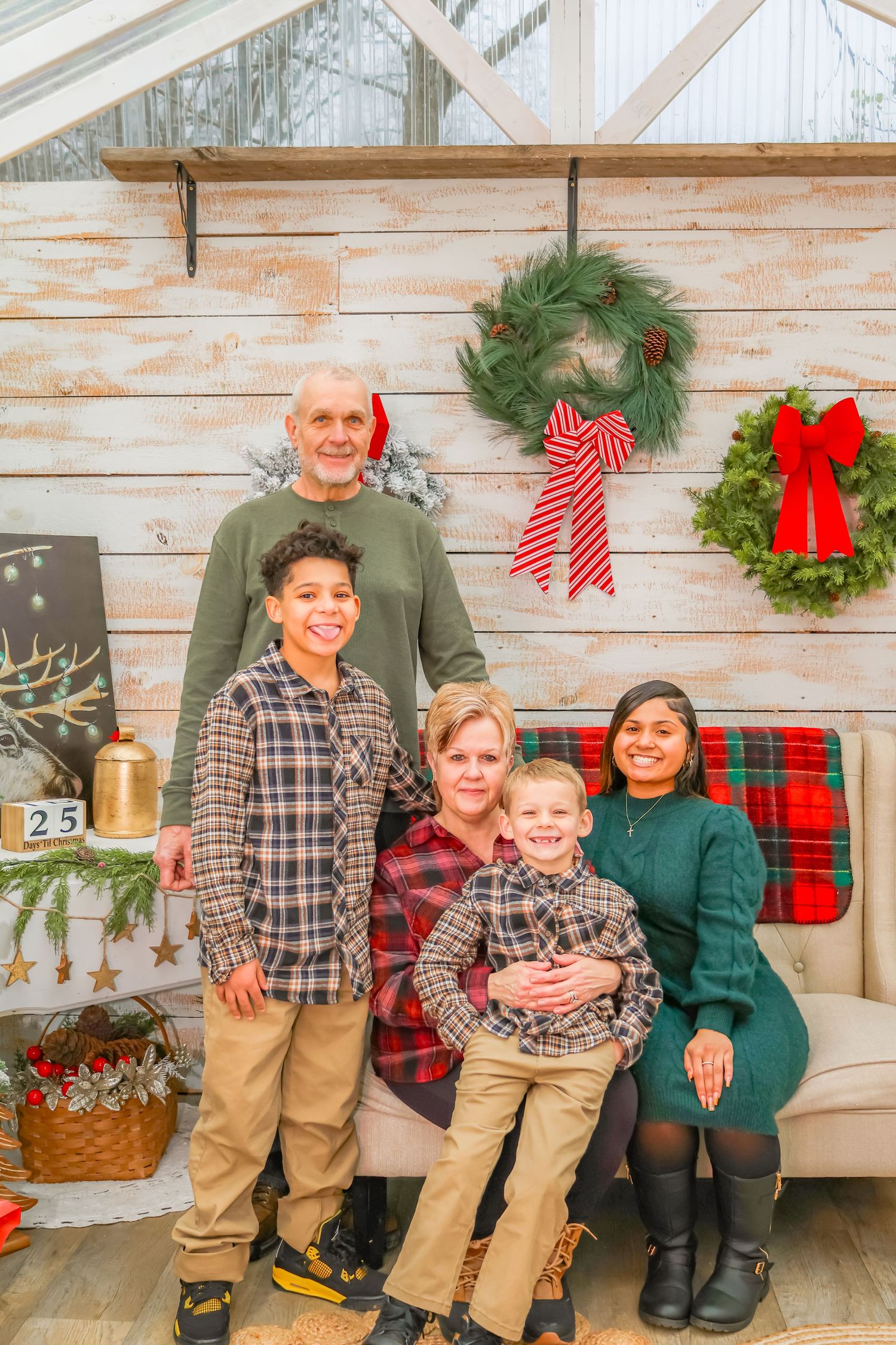 A holiday family portrait against a white wood wall with Christmas wreaths and decorative bows.