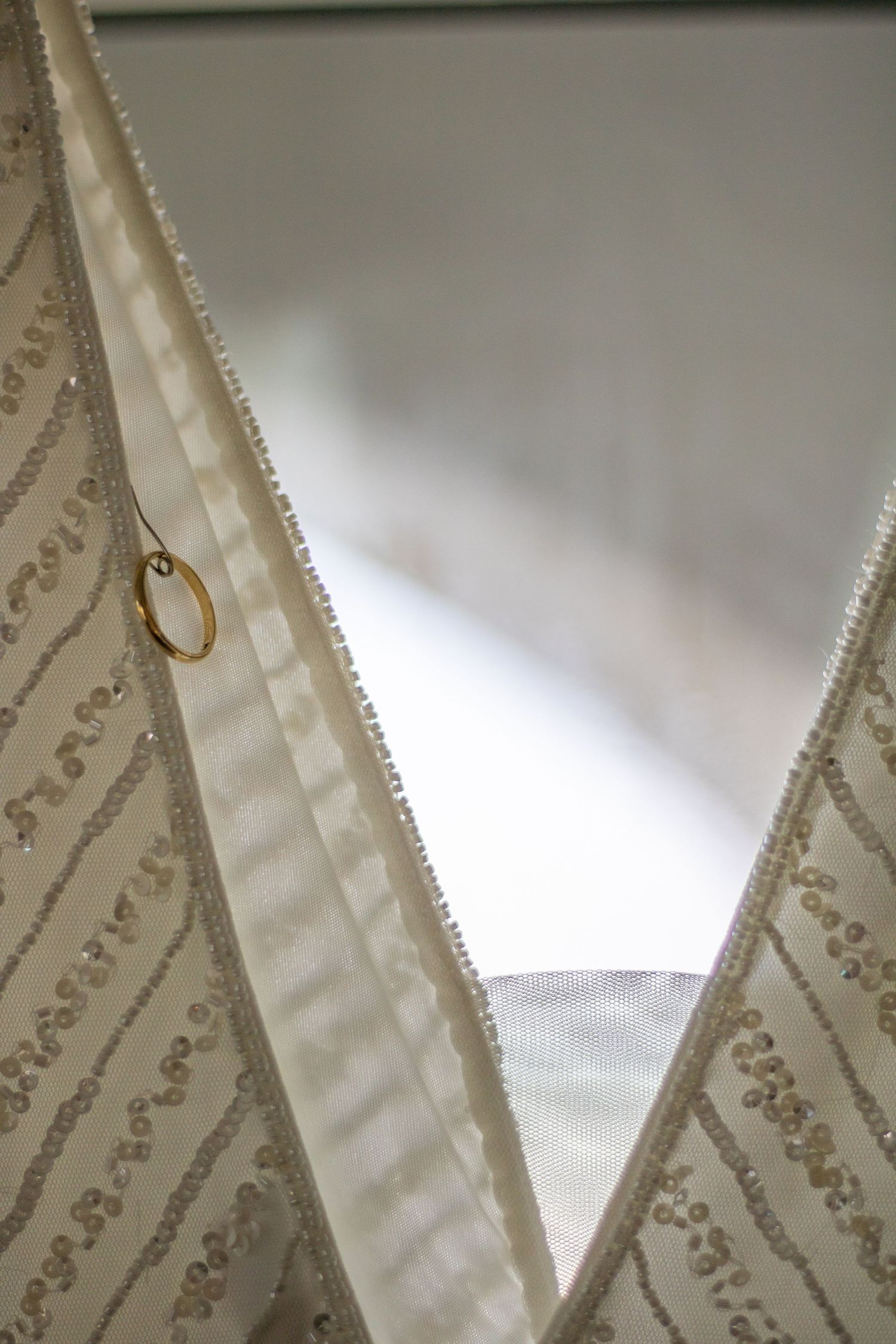 Close-up detail of a wedding dress with beaded pattern and a gold ring.