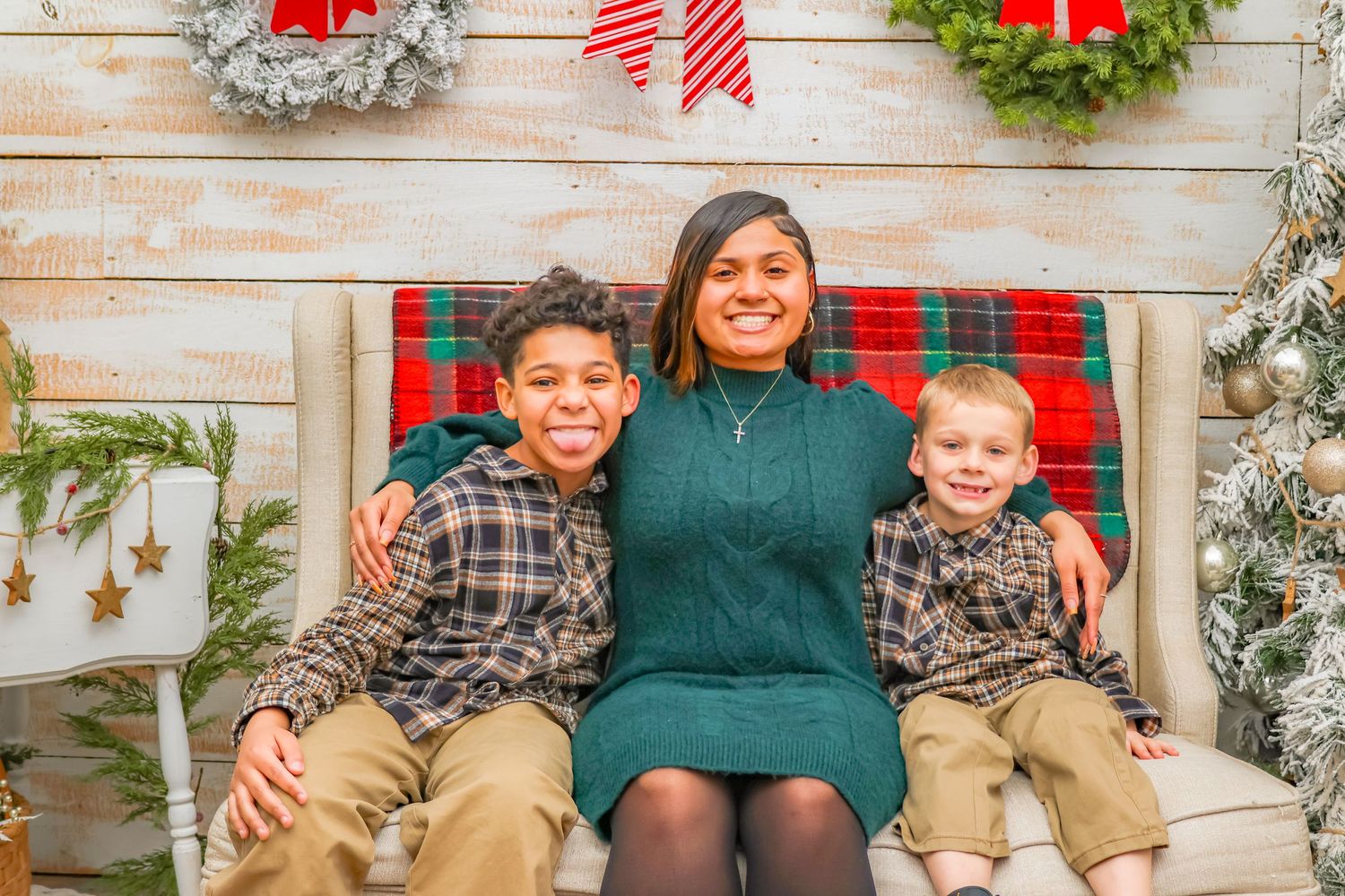 Holiday portrait on plaid bench with wreaths and wooden backdrop.