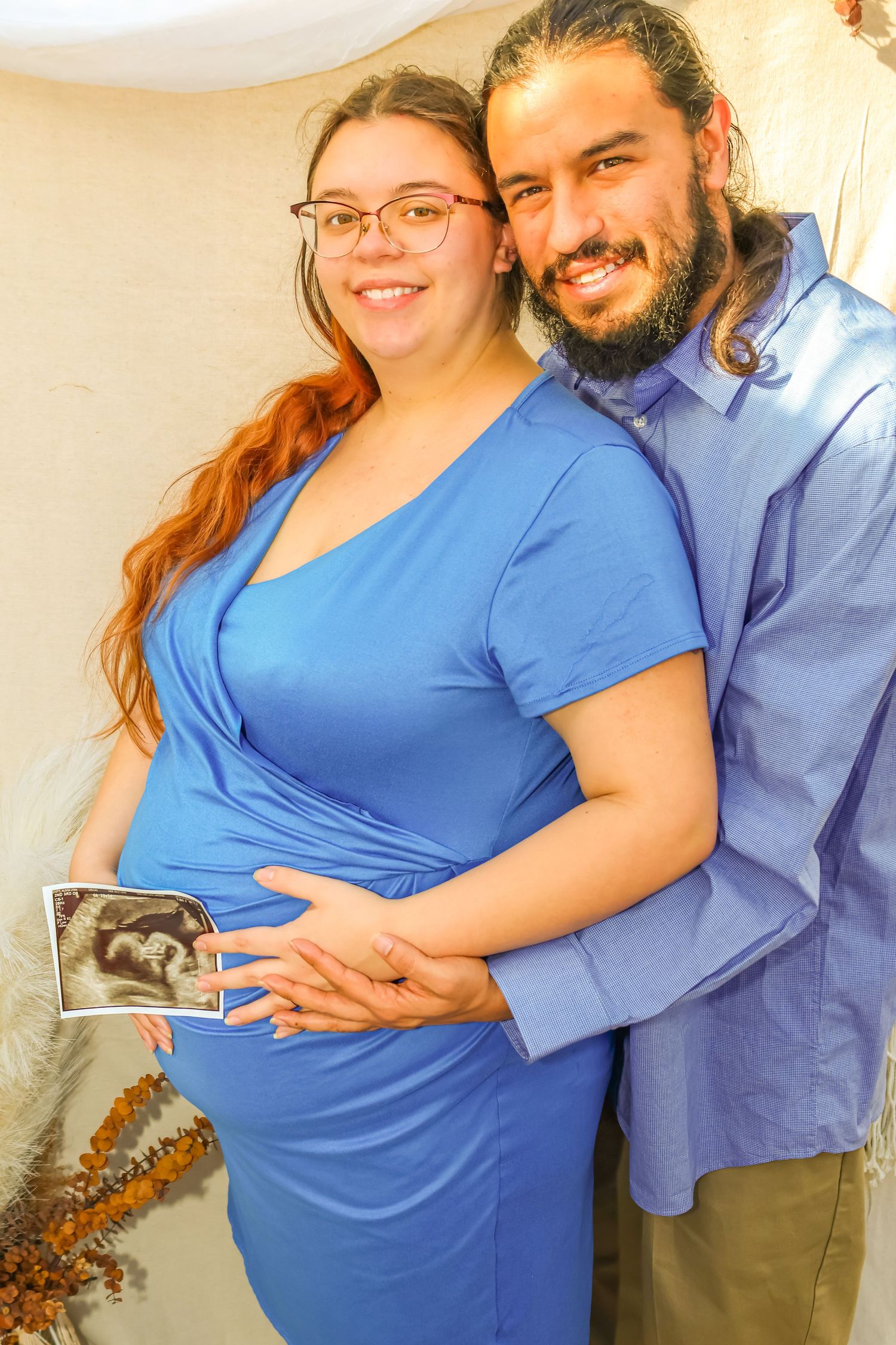 Expecting couple holding ultrasound photo in blue and light blue outfits.