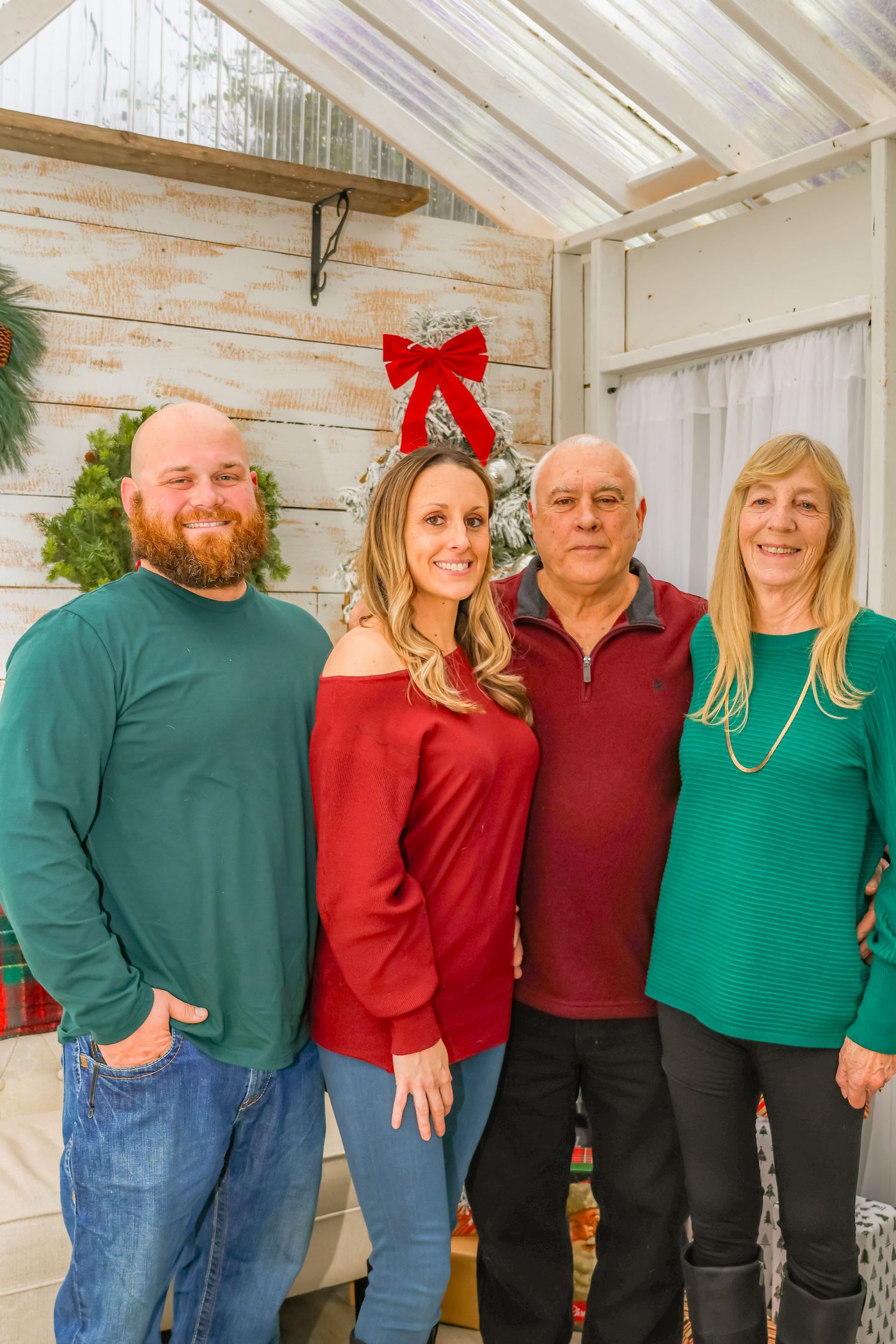 Holiday family photo in coordinating sweaters with Christmas decorations and red bow in background.