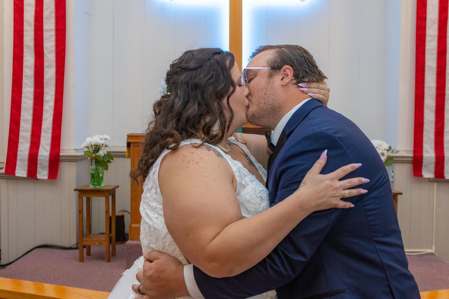 Wedding couple kissing in church with American flags and cross in background.