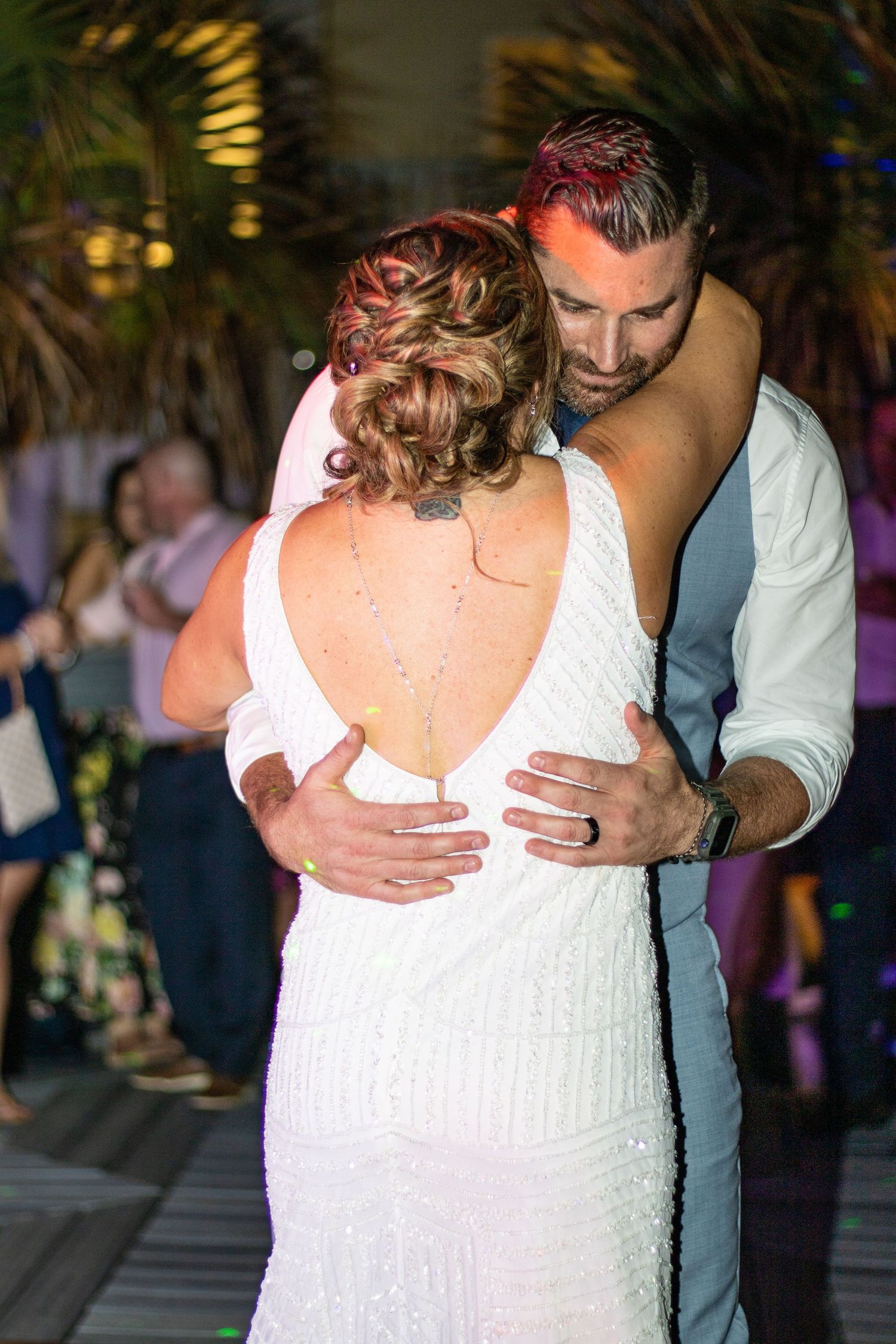 Wedding couple shares a romantic dance at an evening reception with palm trees in the background.