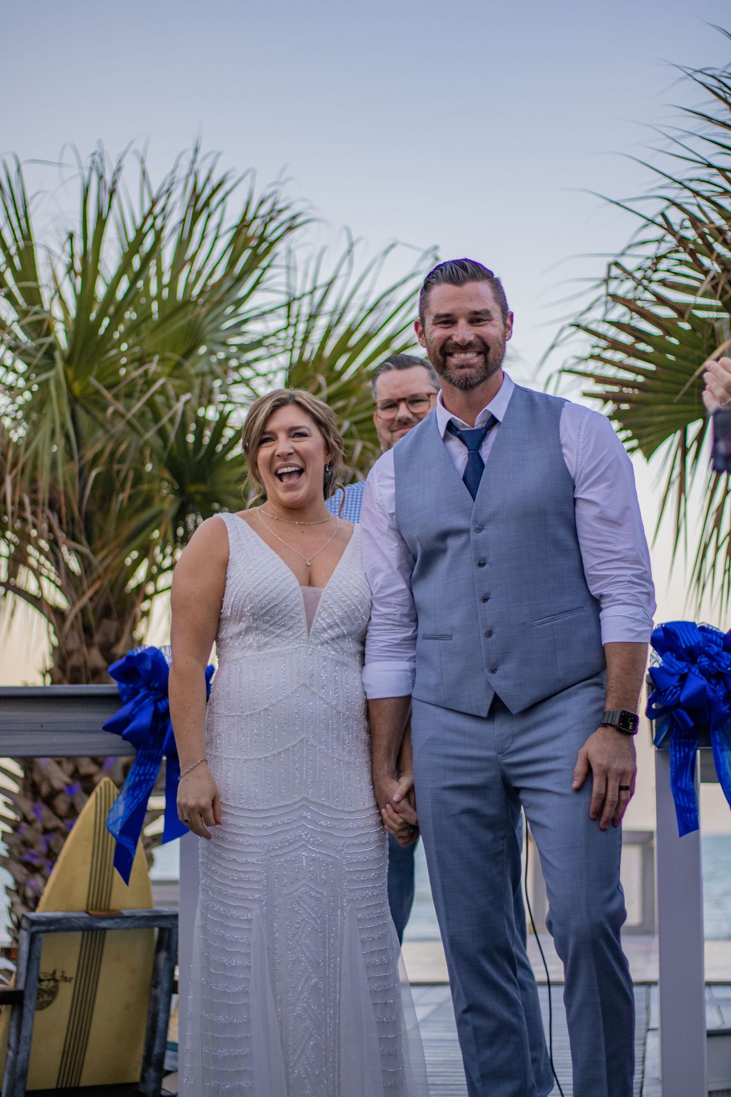 Happy couple celebrates during their beachside wedding ceremony decorated with blue ribbons.
